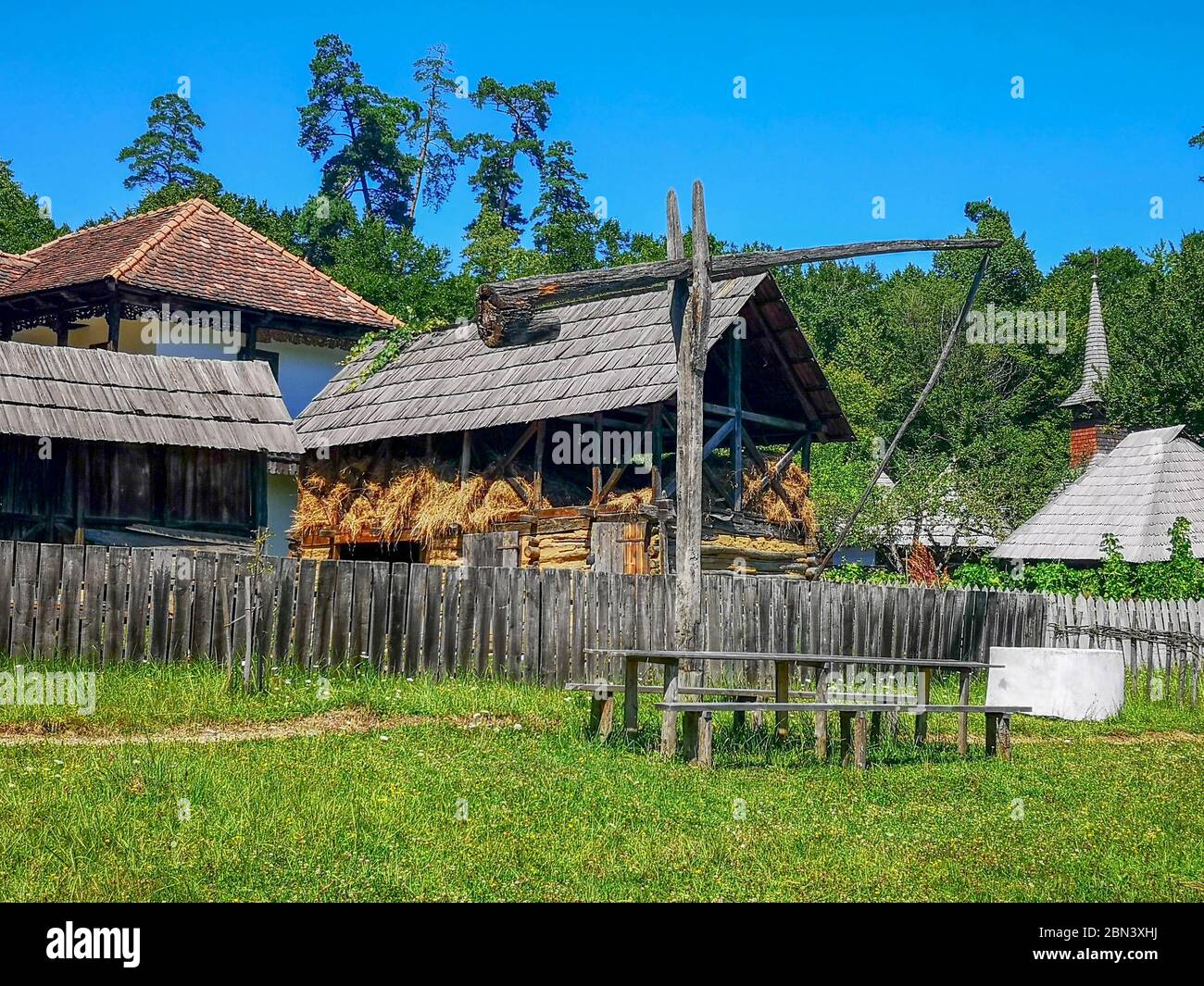 Rustic scene somewhere in the Romanian countryside, with a wooden watershed next to a table with benches and old rural houses with old shingles surrou Stock Photo