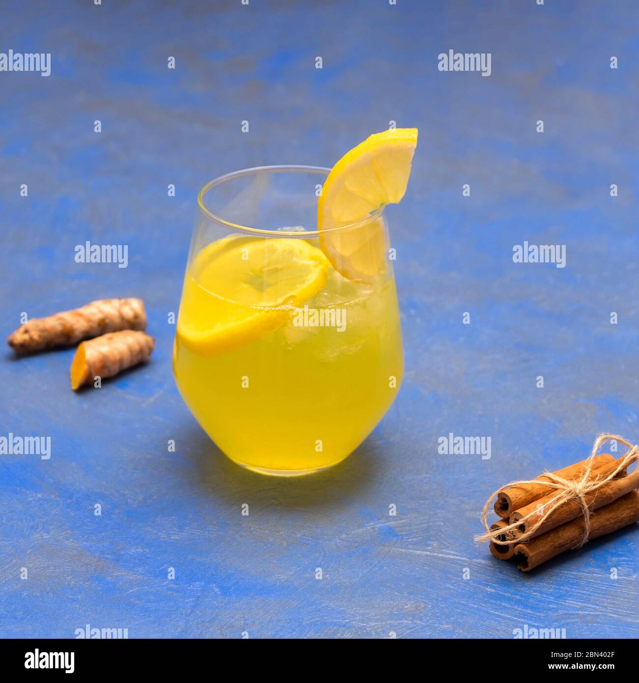 Homemade turmeric-ginger iced tea with cinnamon and lemon in a glass cup on blue background Stock Photo