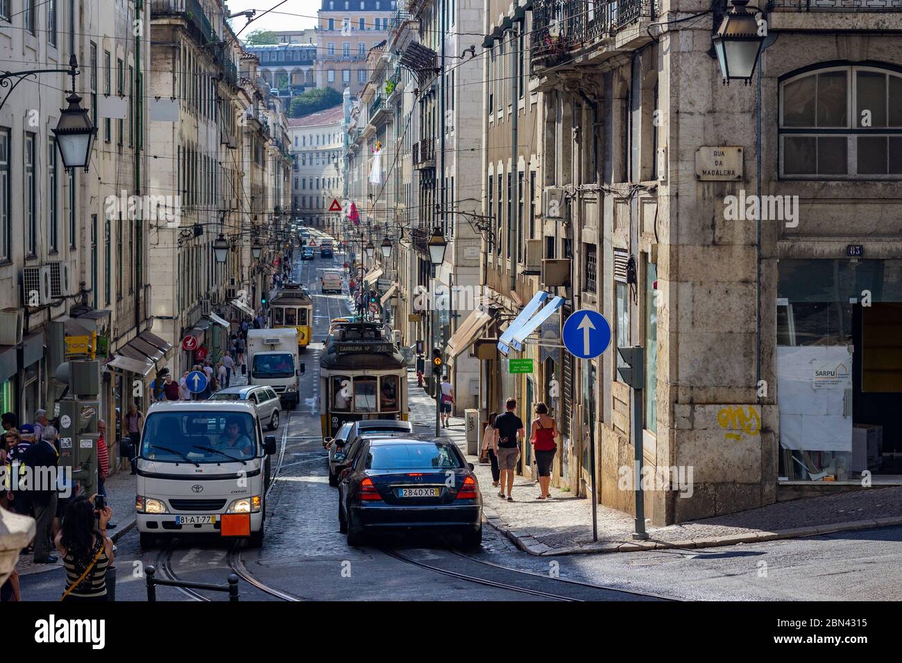 Cars, tourists, and a streetcar can be seen down a narrow street in
