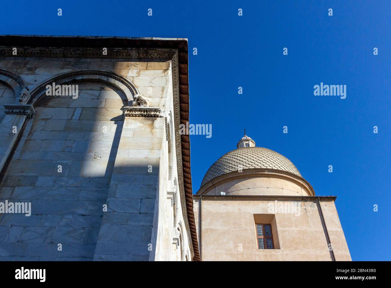 A corner of the Pisa Cathedral is illuminated by the sun against a clear-blue sky in Pisa, Italy Stock Photo