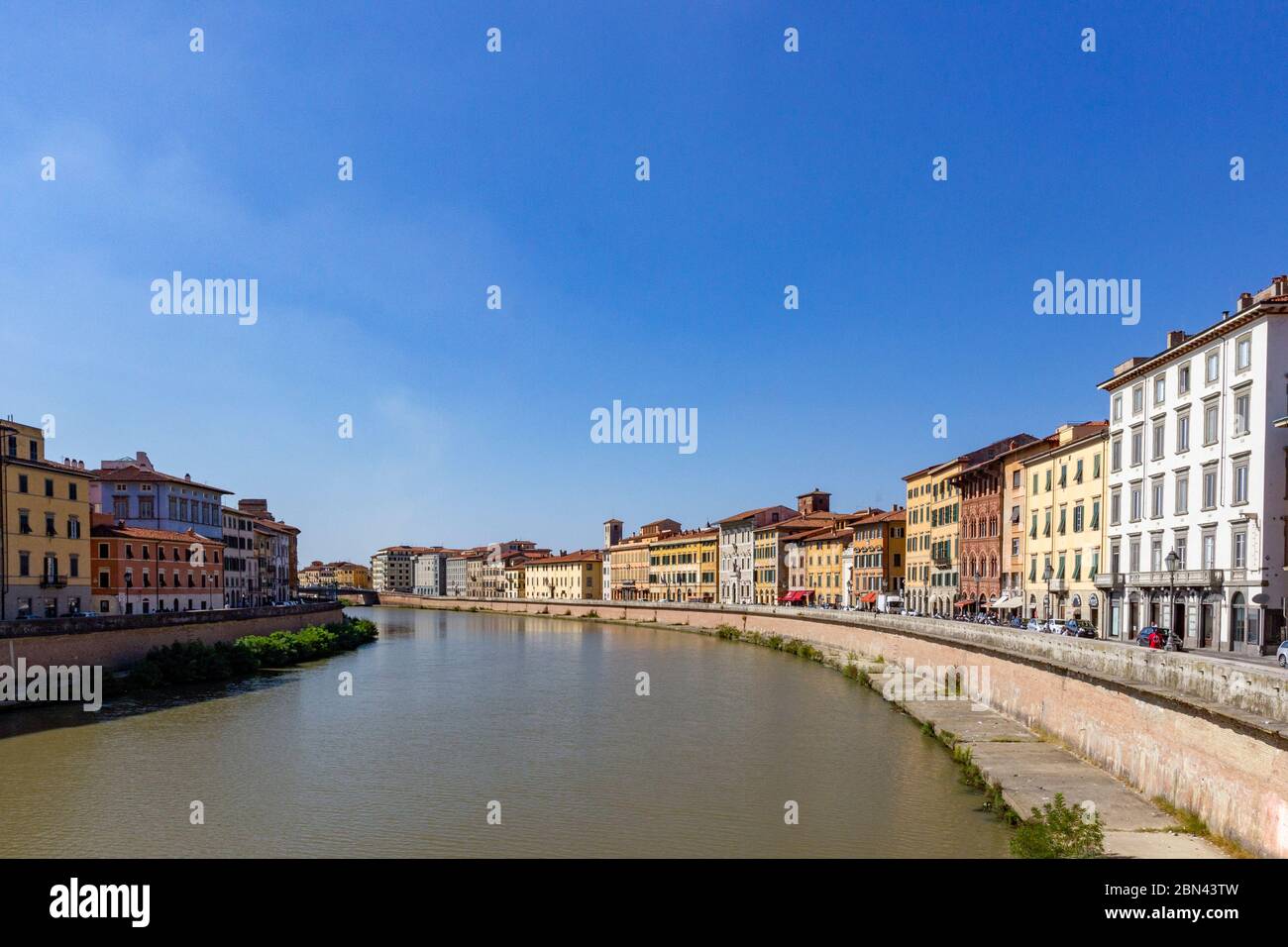 The Arno river bends through the city of Pisa, Italy, surrounded on both sides by a concrete wall and sunlit buildings Stock Photo