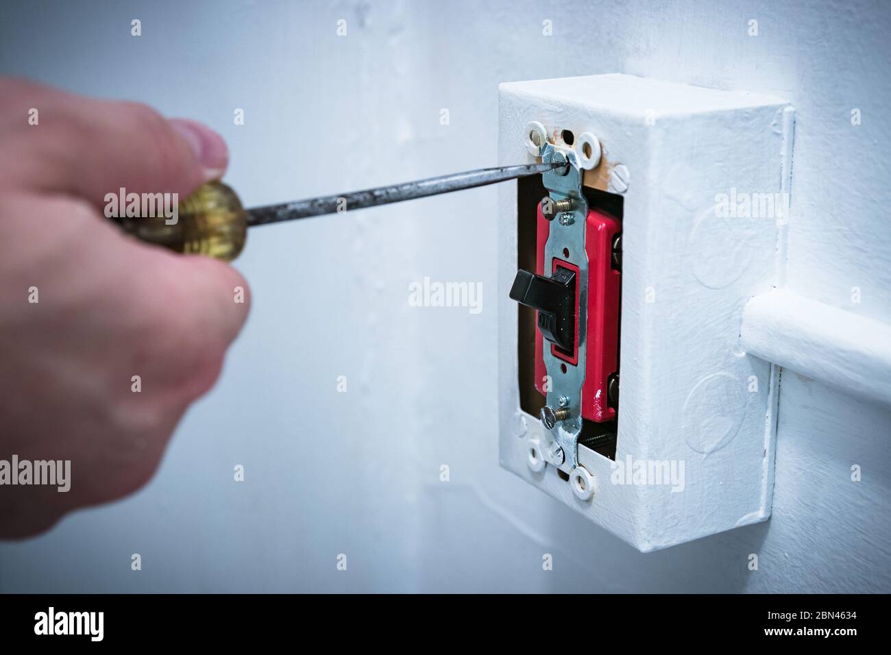 Man's hand using screwdriver to replace/repair 20 amp lightswitch on wall. Stock Photo