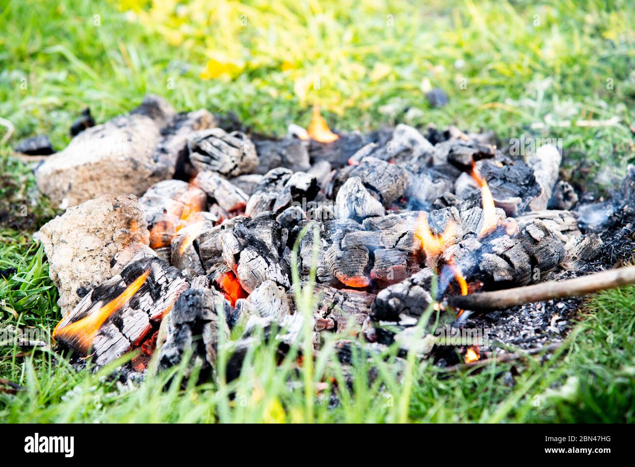 burning coal from a fire on green grass Stock Photo