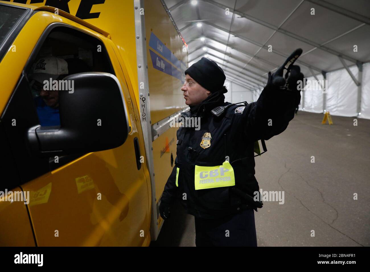 A U.S. Customs and Border Protection, Office of Field Operations, officer gestures as he directs the driver of a truck where to stand shortly before X-raying the vehicle during non-intrusive inspections prior to Super Bowl LII in Minneapolis, Minn., Jan. 30, 2018. On Sunday, Feb. 4, the Philadelphia Eagles will face off against the New England Patriots for the NFL championship title. U.S. Customs and Border Protection Stock Photo