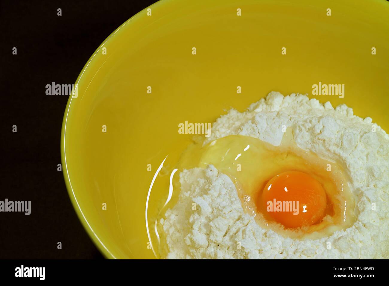 Closeup cracked egg on raw flour in a yellow mixing bowl Stock Photo