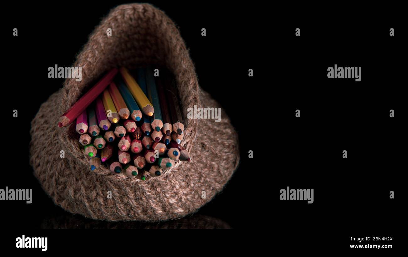 colored pencils in a knitted basket on a black background Stock Photo