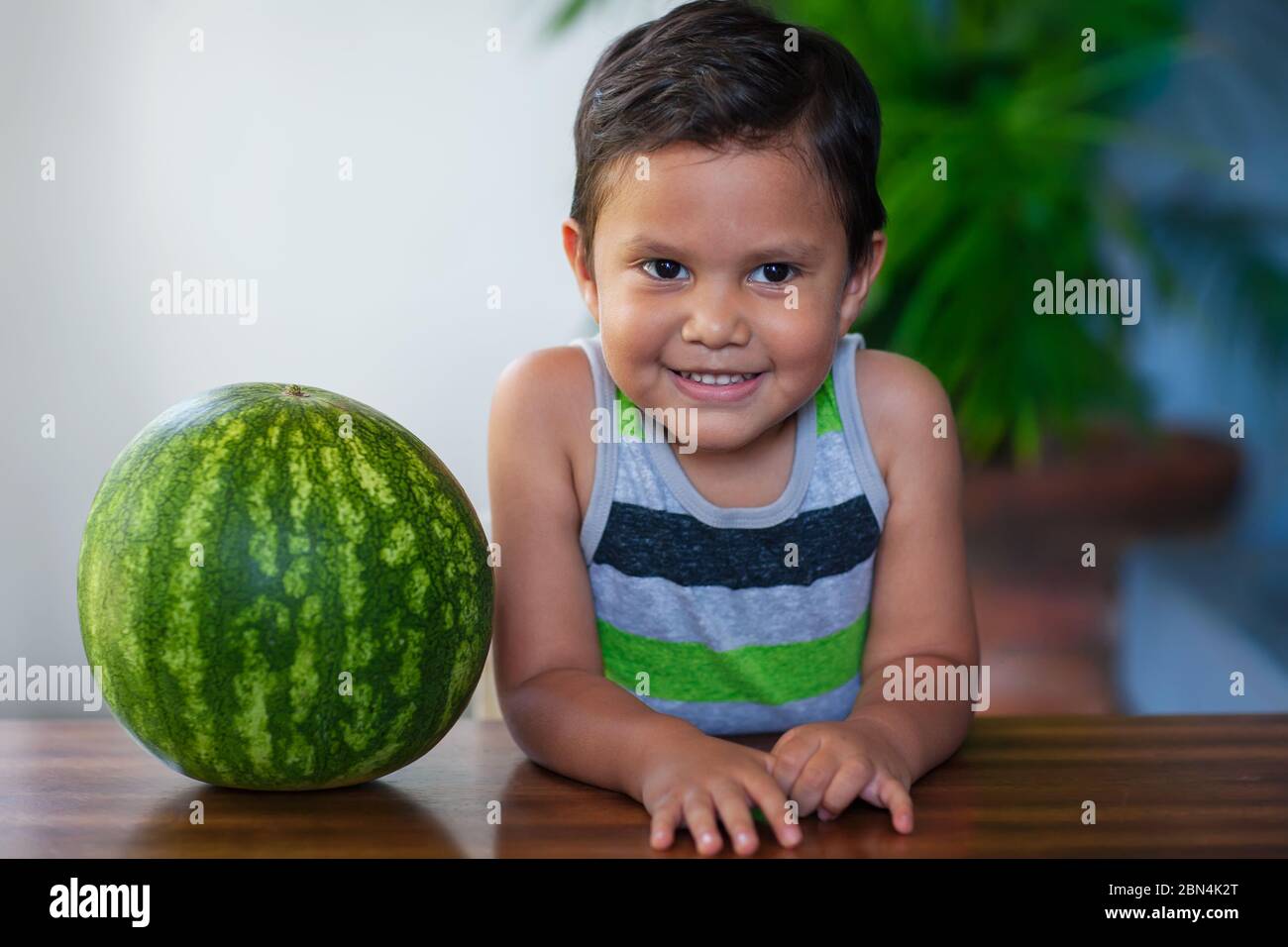 A cute young boy sitting next to a ripe watermelon he will be eating as part of a low-calorie and nutritious treat. Stock Photo