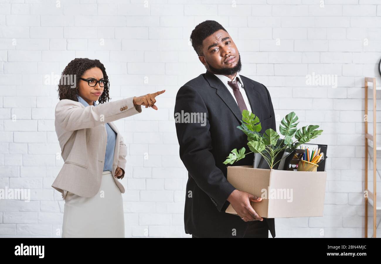 Young black businessman with cardboard box being fired by frustrated female boss at office Stock Photo