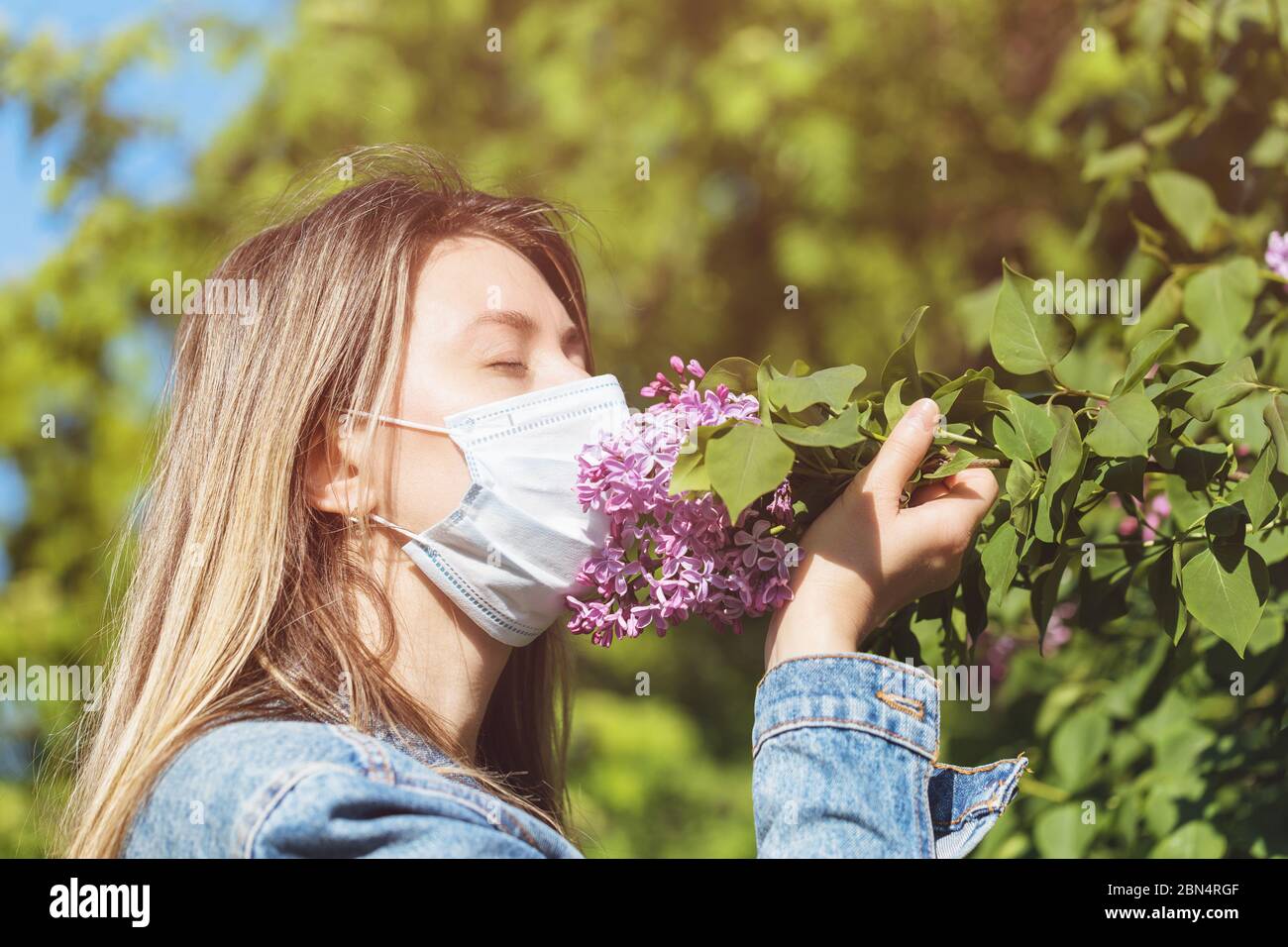 The girl in the mask sniffs a lilac on the street. Concept on quitting quarantine Stock Photo