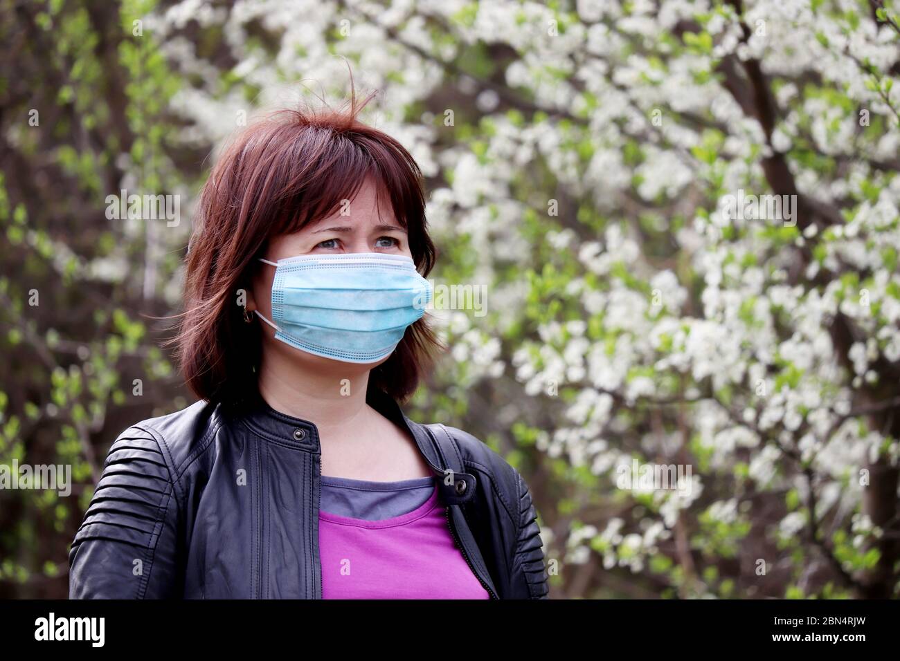 Woman in medical protective mask in a spring garden on cherry blossom background. Concept of quarantine during covid-19 coronavirus pandemic Stock Photo