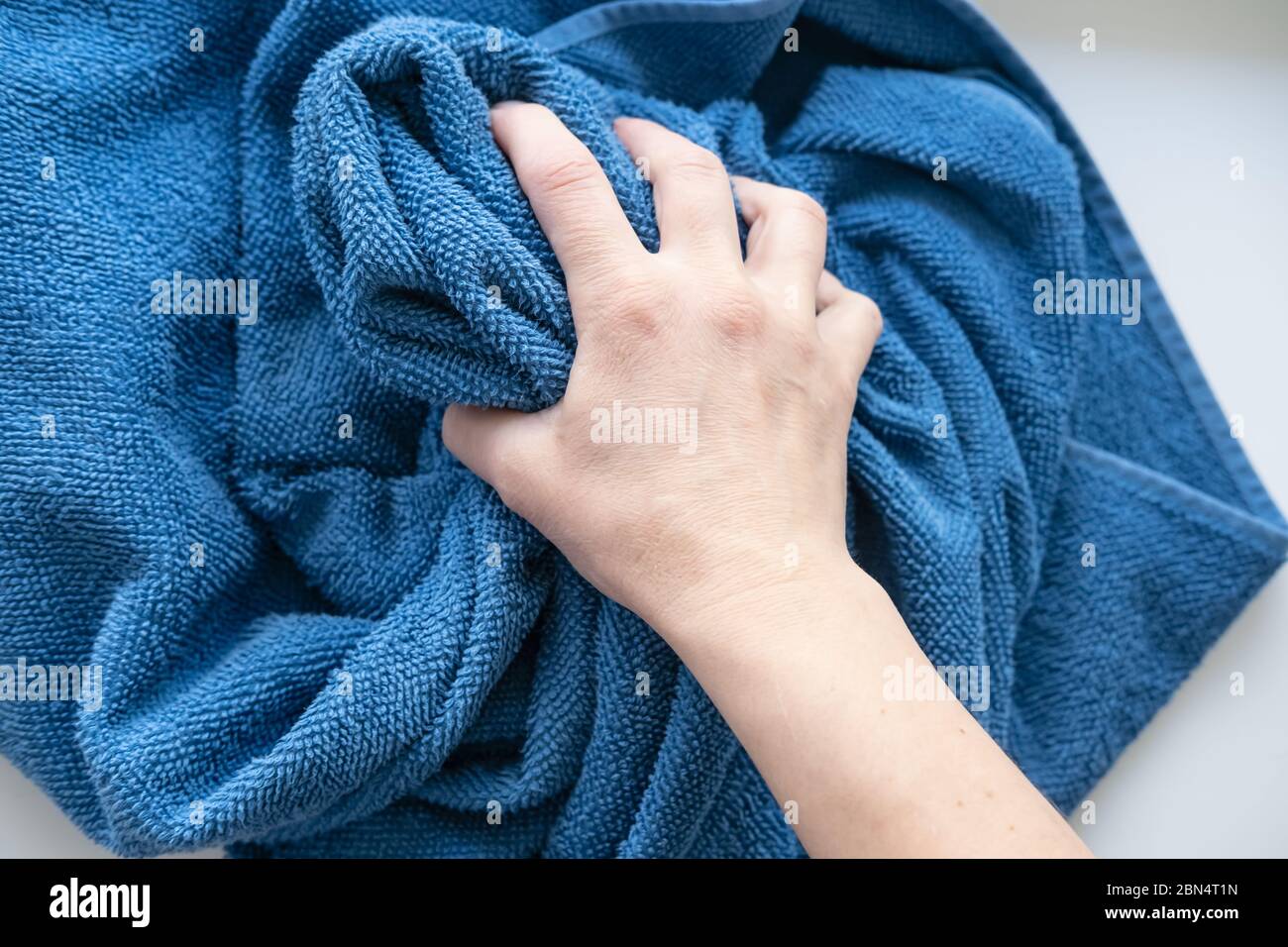 Hand takes crumpled terry, blue towel on white textured surface. Top view. Stock Photo