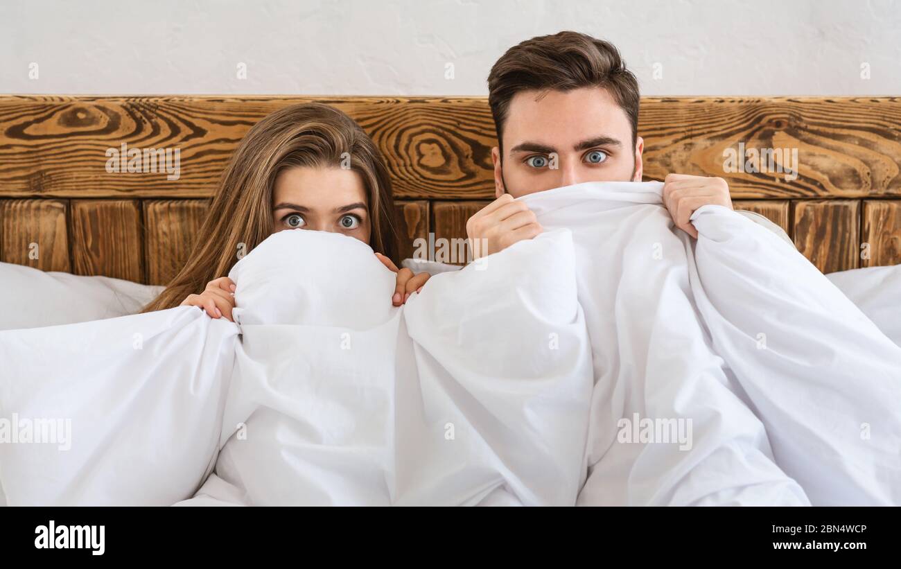 Fear concept. Husband and wife hiding at blanket and watching movie