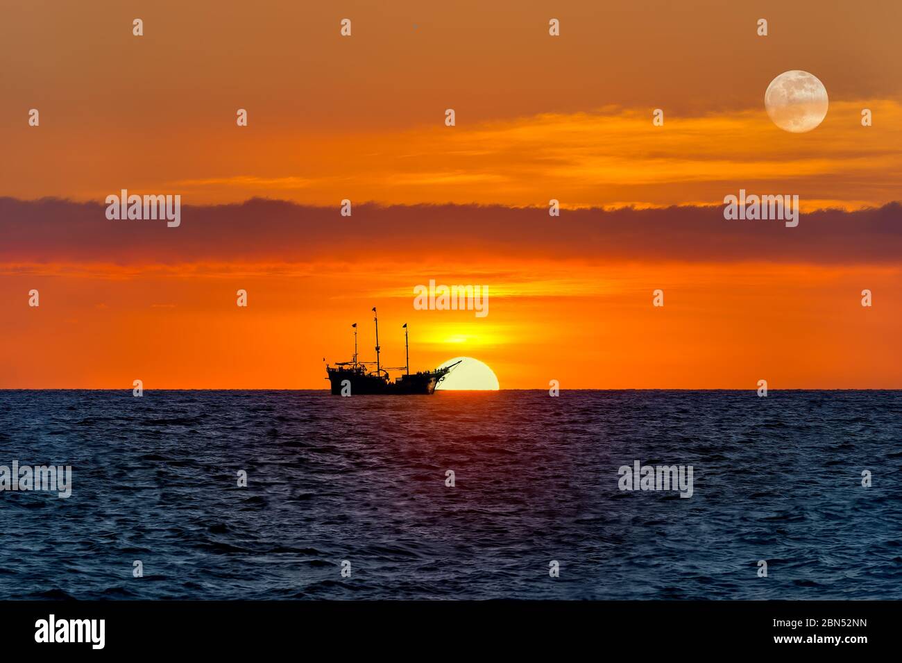 An Old Wooden Ship Sits at sea as the Sun Goes Down on the Ocean Horizon and the Moon Rises in the Sky Stock Photo