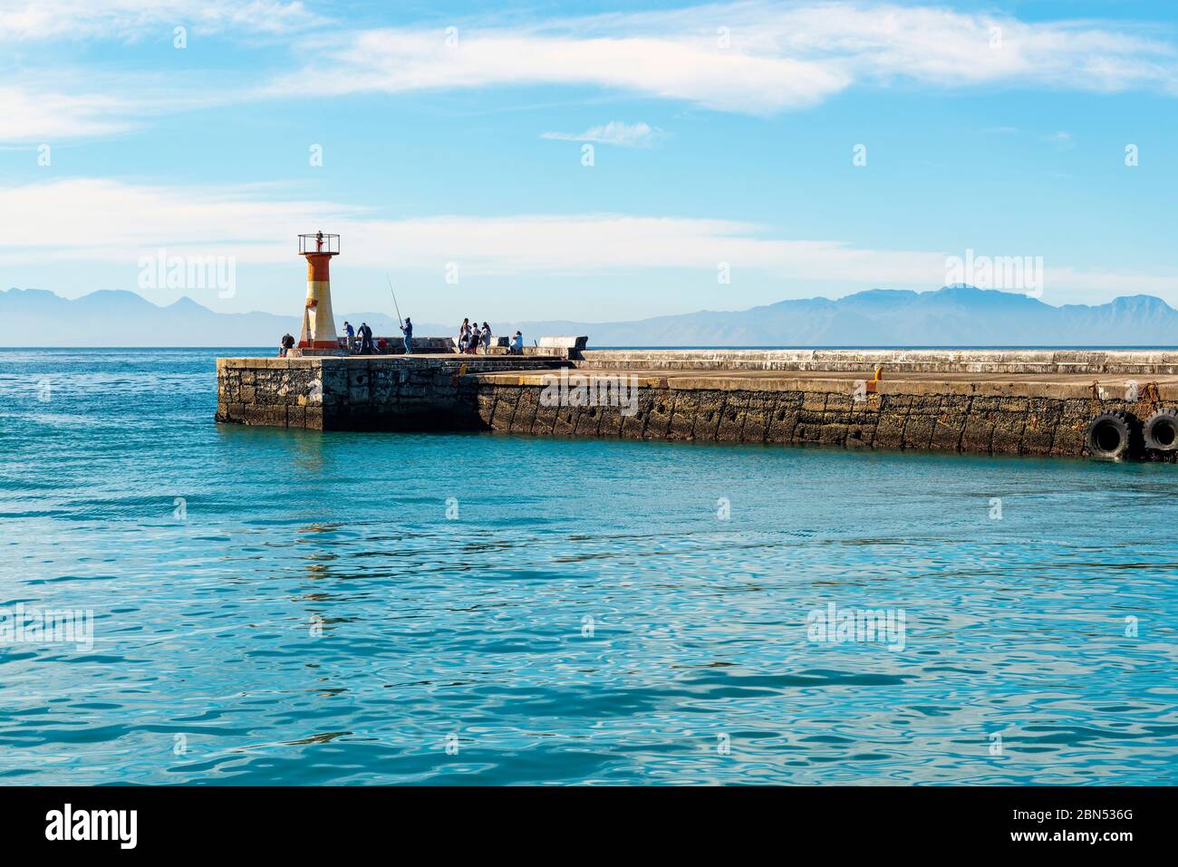 Fishermen and people walking by the lighthouse of Kalk Bay harbor near Cape Town, South Africa. Stock Photo