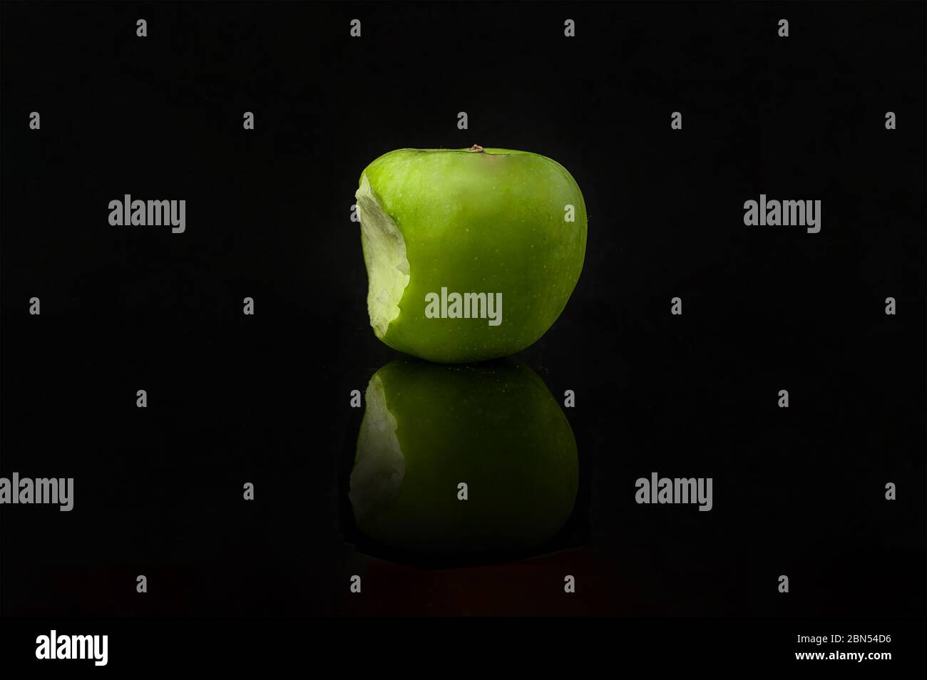 Bitten green apple with reflection on black background. Stock Photo
