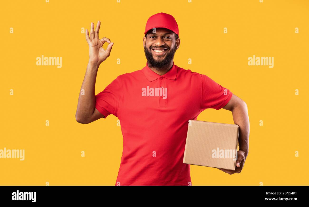 Courier Guy Holding Cardboard Box Gesturing Okay On Yellow Background
