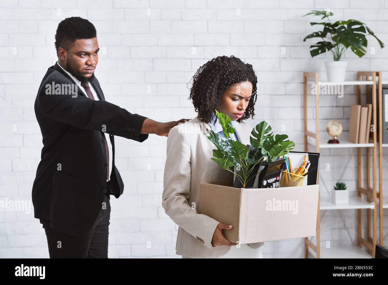 Losing job concept. Strict African American boss and unhappy female employee with box of things at office Stock Photo