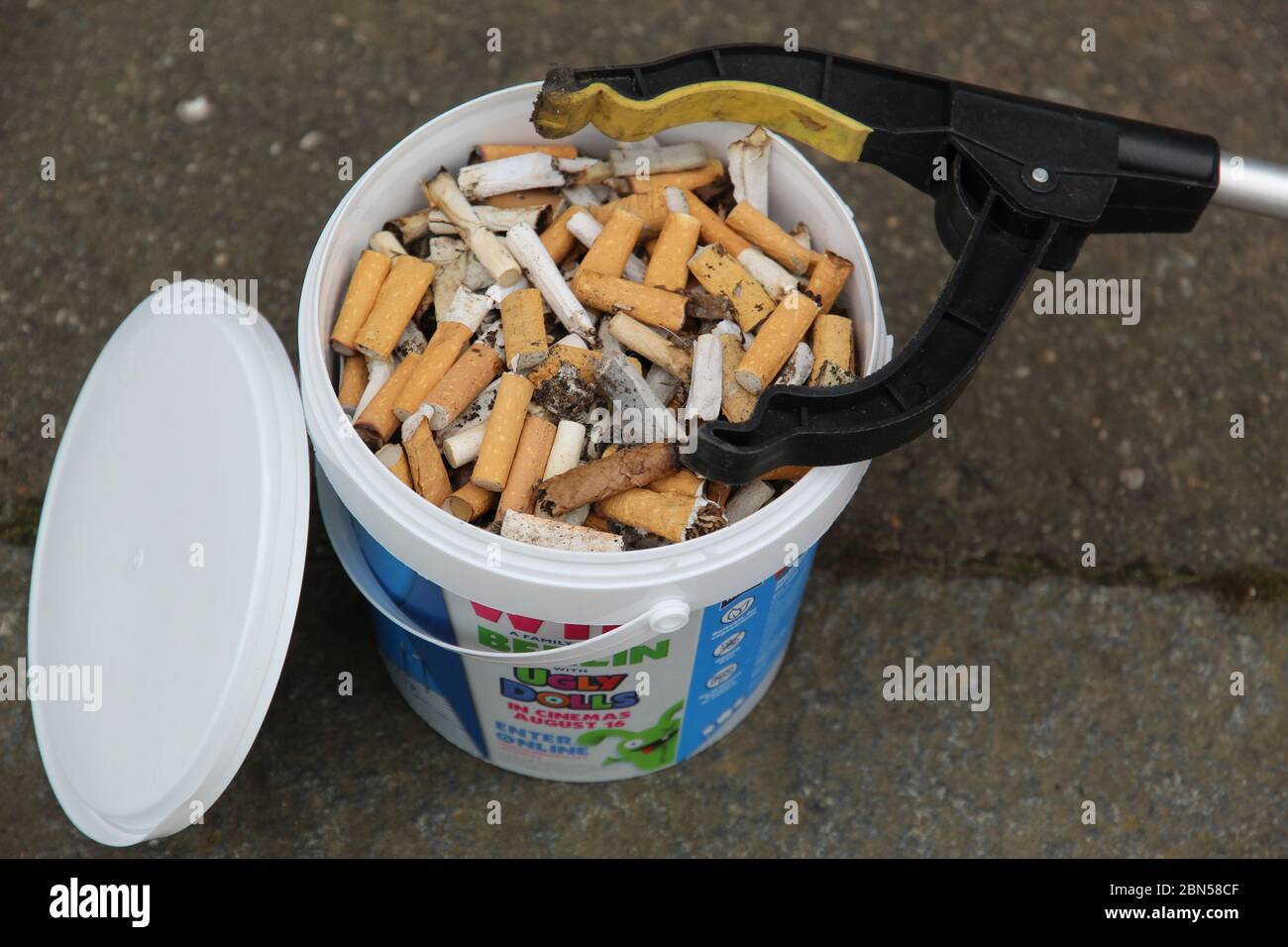 Large Yoghurt Tub Filled with Cigarette Ends and a Litter Picker Stock Photo