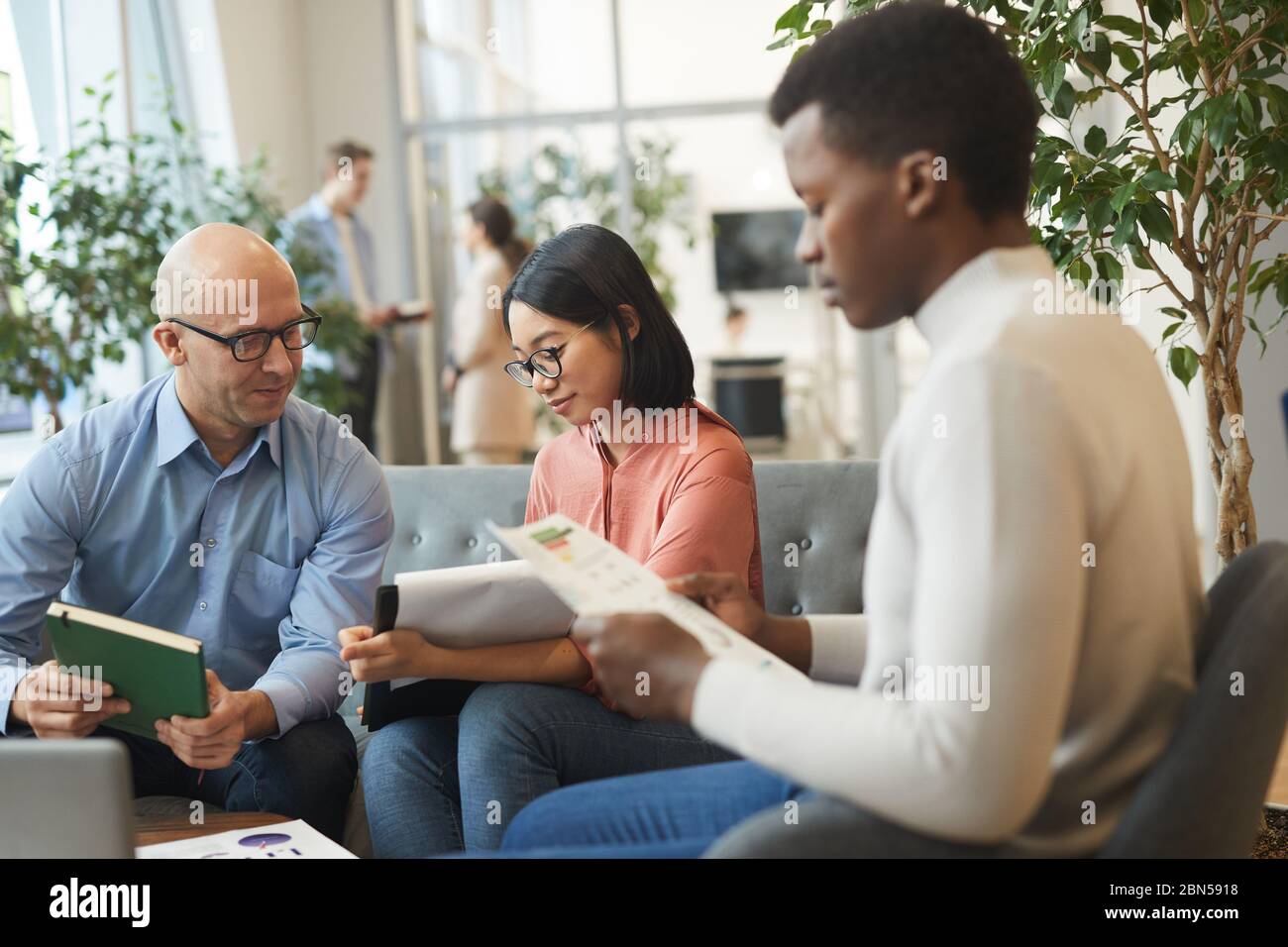Portrait of multi-ethnic business team working on project in office, focus on smiling Asian businesswoman holding clipboard, copy space Stock Photo