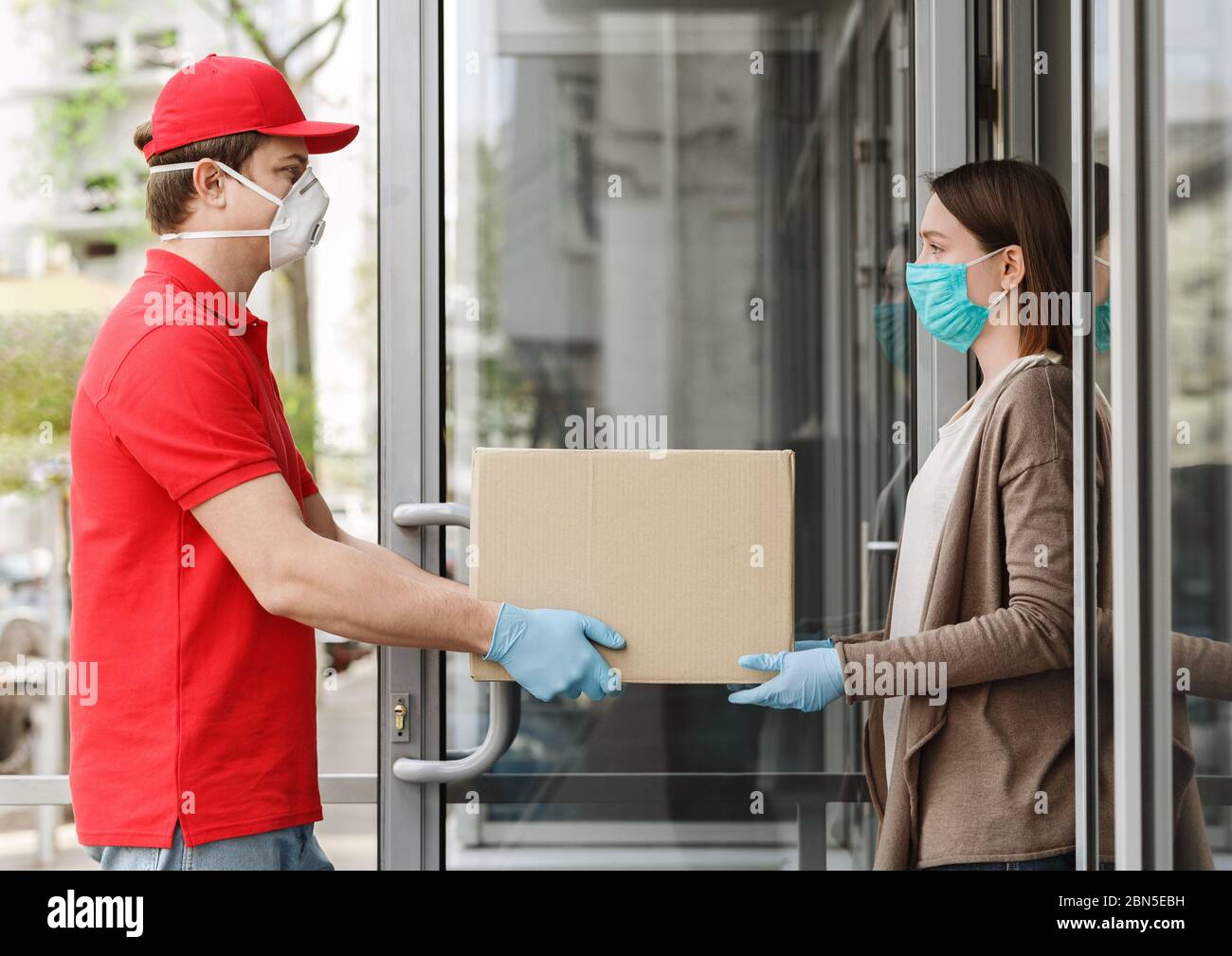 Girl opens door and takes box from the courier, in protective mask and gloves Stock Photo