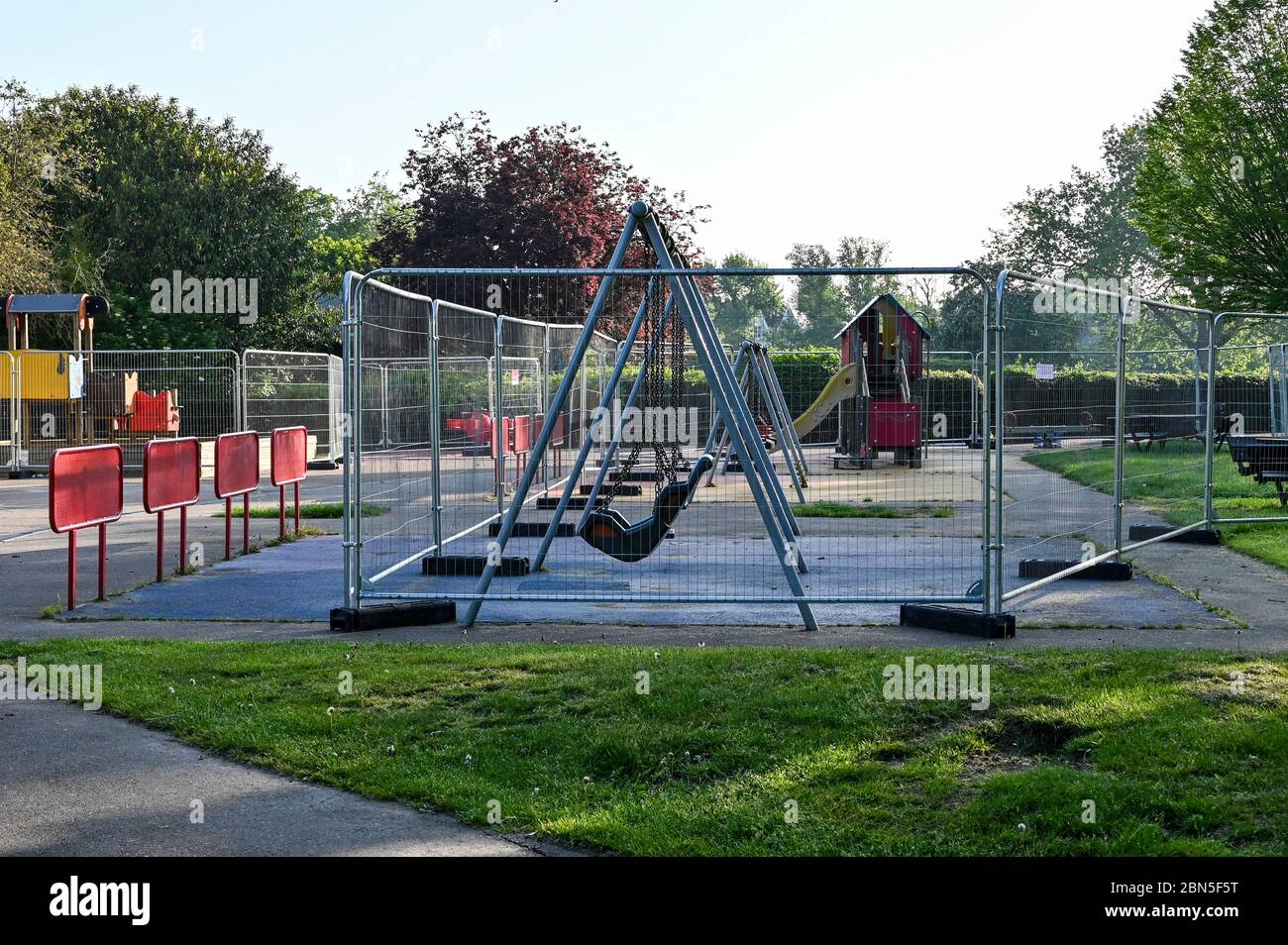 Childrens swings in a playground or play park surrounded by barriers during the coronavirus pandemic. Stock Photo
