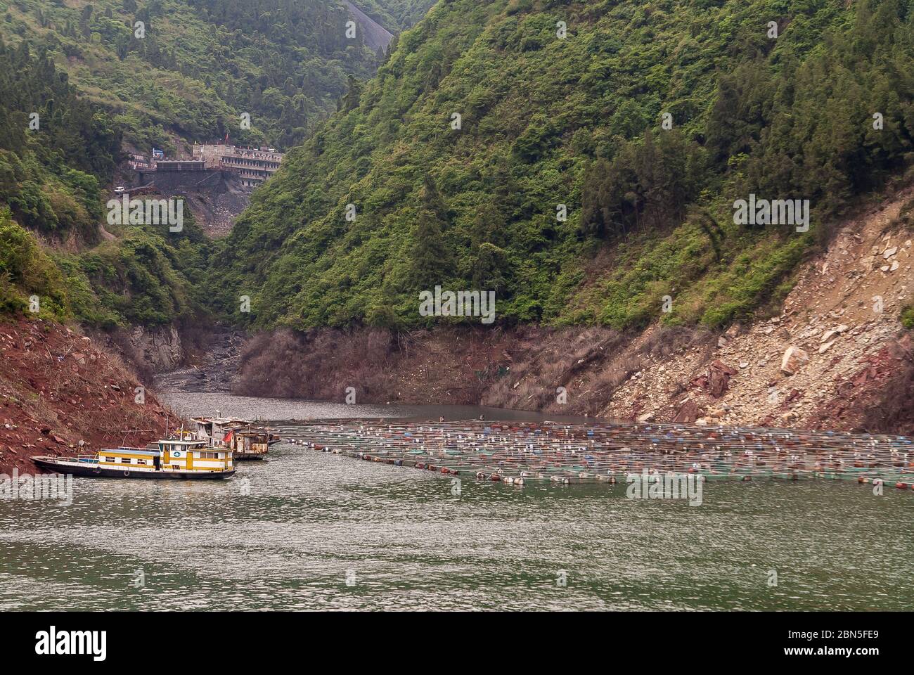 Xinling, China - May 6, 2010: Xiling gorge on Yangtze River. Large fish pen operation with small boats along shoreline at water canyon between steep g Stock Photo