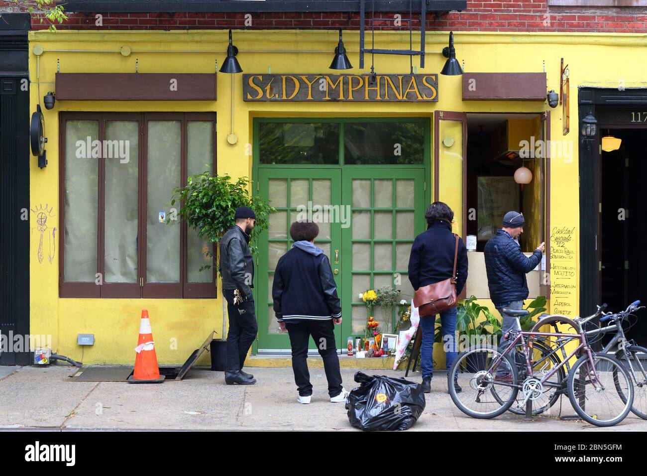 People in front of St. Dymphnas bar in New York's East Village for takeaway drinks during coronavirus. A memorial for a worker unrelated to covid 19 Stock Photo