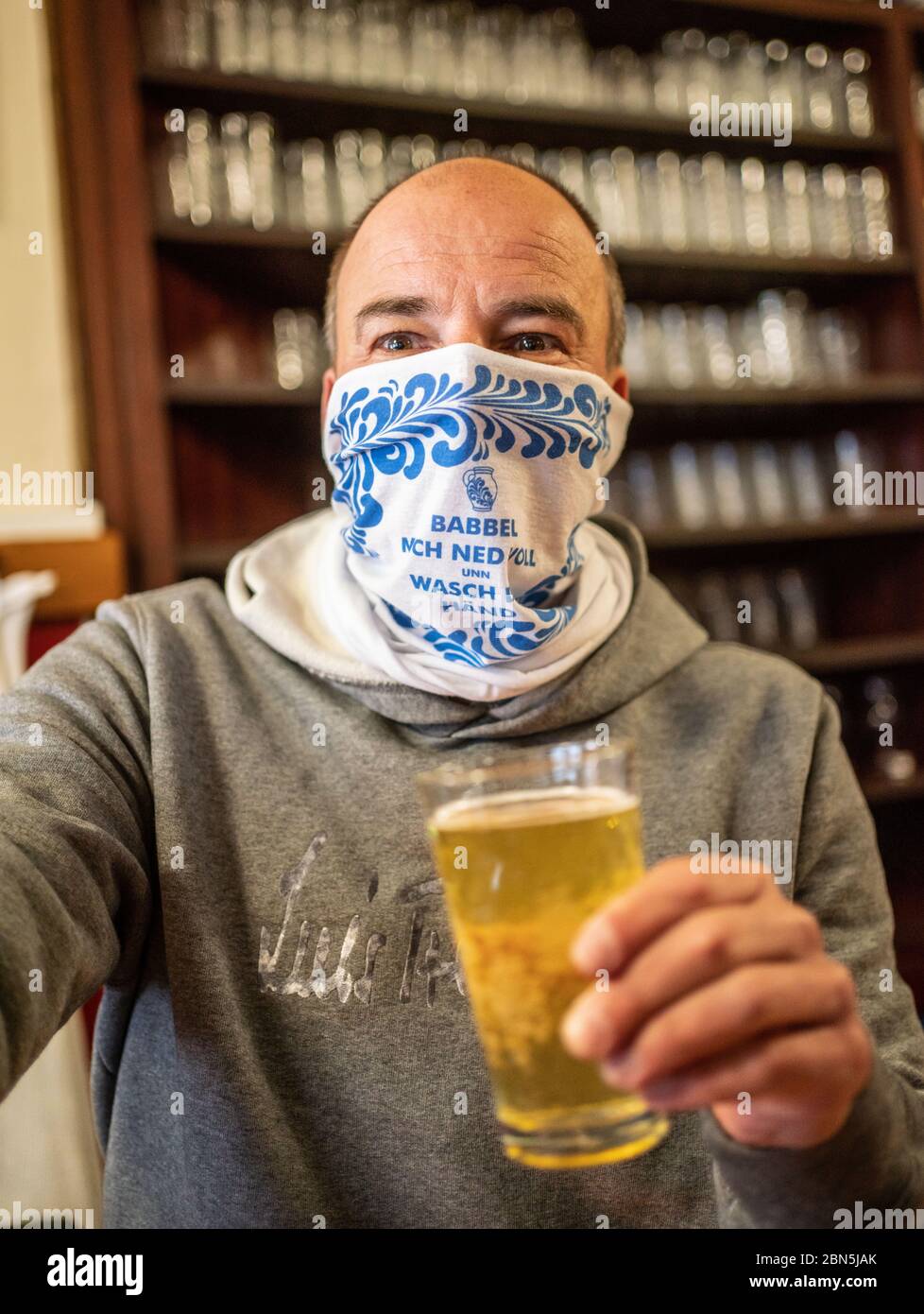 12 May 2020, Hessen, Frankfurt/Main: Ralf Wagner (53), owner of the cider bar 'Wagner', stands behind the counter with a face cloth with the Hessian inscription 'Babbel mich ned voll unn wasch dei Händ' (Don't talk me full and wash your hands). Due to the Corona pandemic, the traditional company still only offers take-away food. From this Friday (15.05) restaurants, cafés and pubs in Hesse are allowed to open to the public again. Hygiene and distance regulations must be observed. Photo: Frank Rumpenhorst/dpa Stock Photo