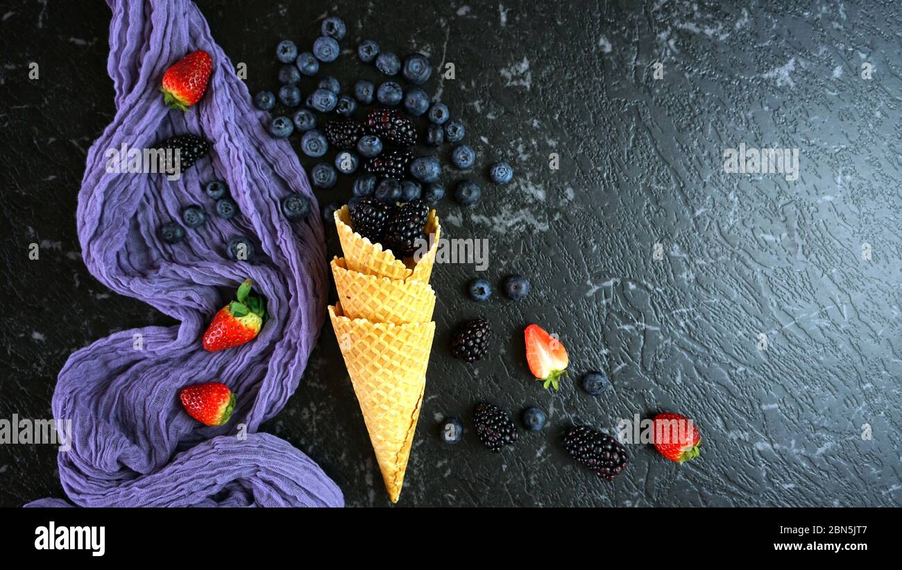 Summer berries creative flatlay top view with blueberries and blackberries in ice cream waffle cone. Dark moody creative composition with negative cop Stock Photo