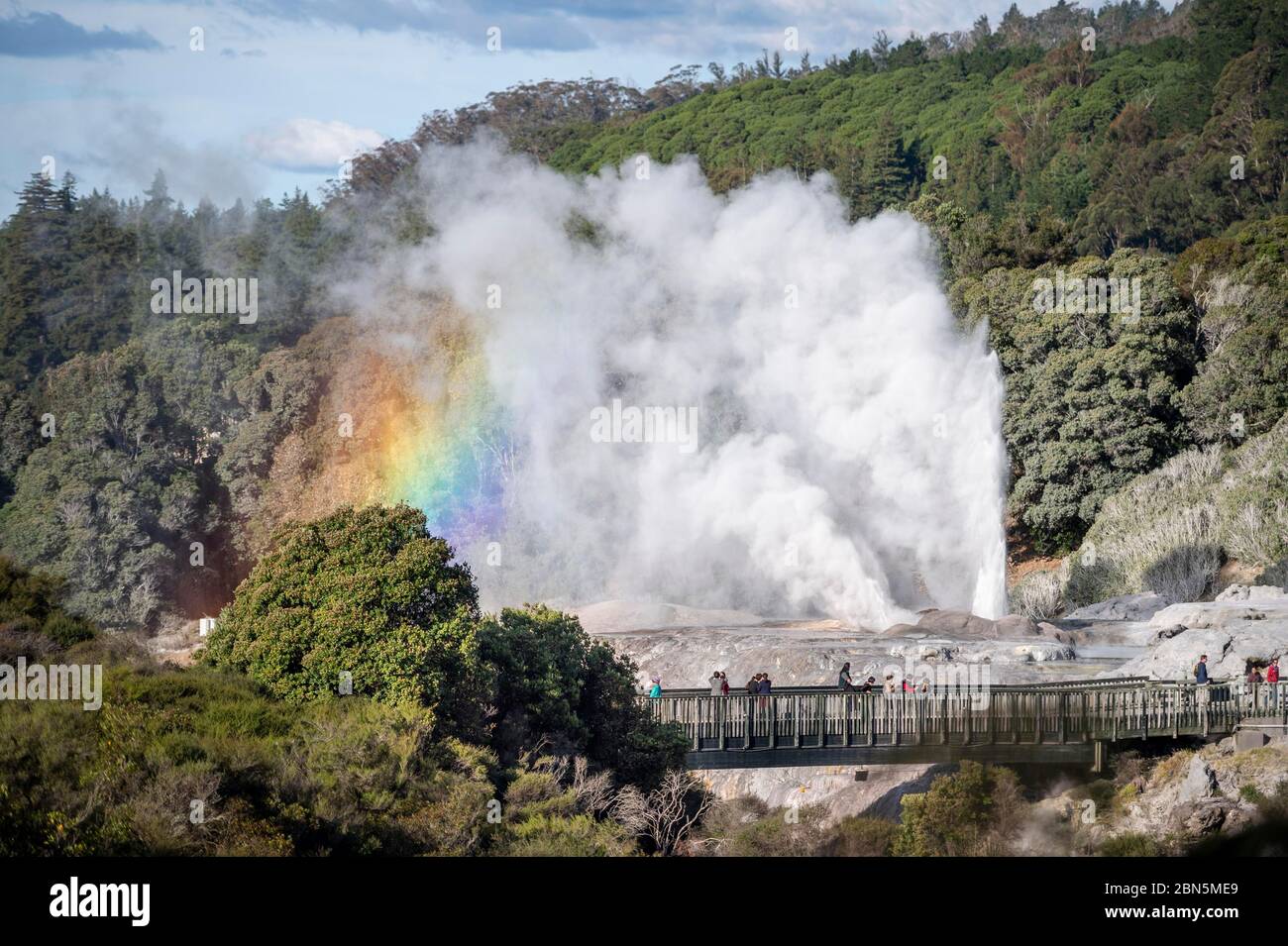 Tourists on bridge, view of erupting Pohutu Geyser with rainbow, Te Puia, Whakarewarewa, Rotorua, Bay of Plenty, New Zealand Stock Photo