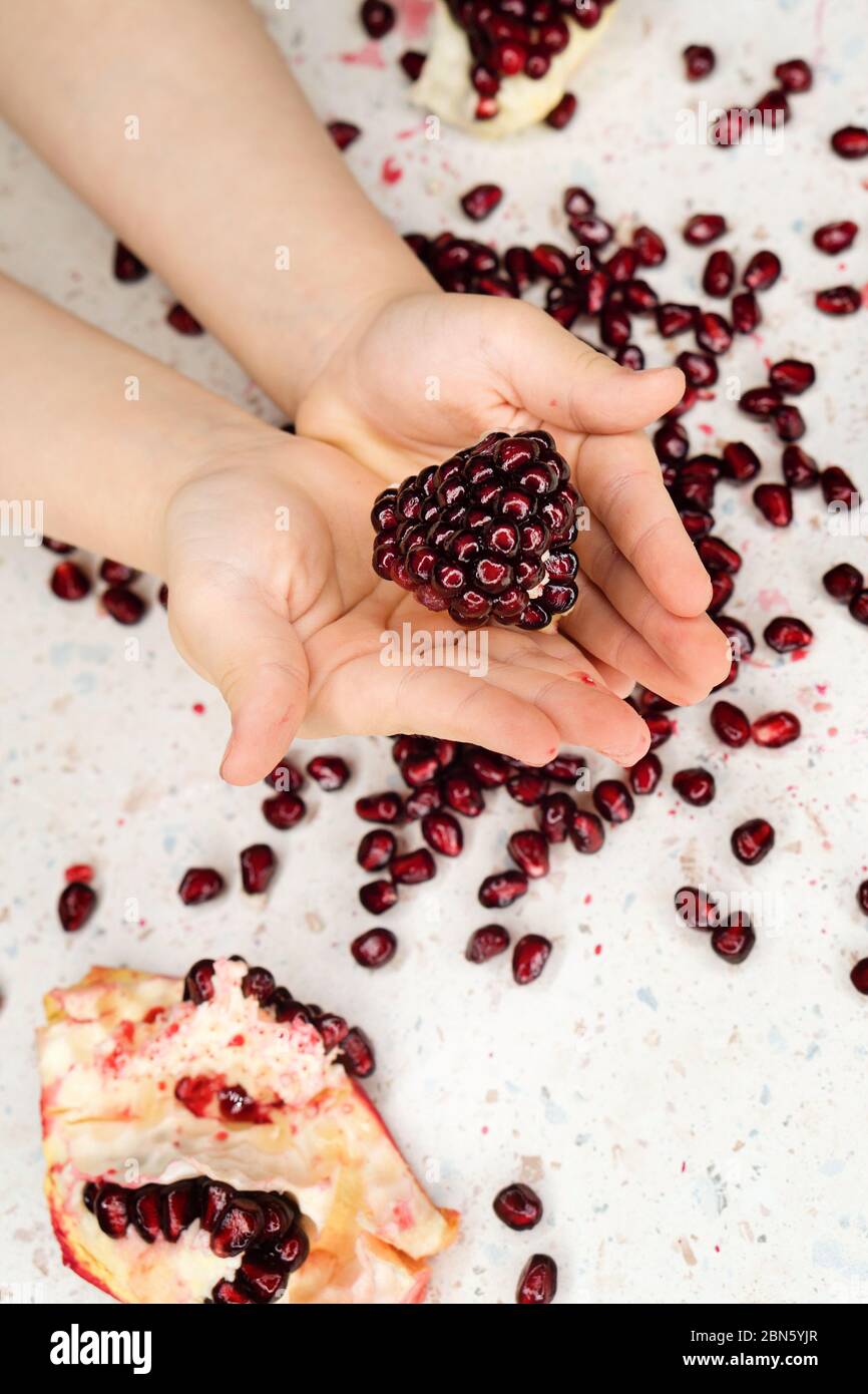 Child holding and showing in his hands pomegranate, white table