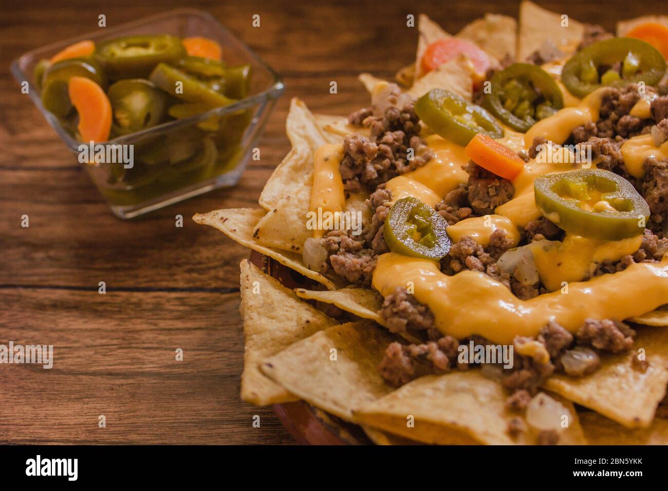 nacho chips corn garnished with ground beef, melted cheese, chili peppers in plate on wooden