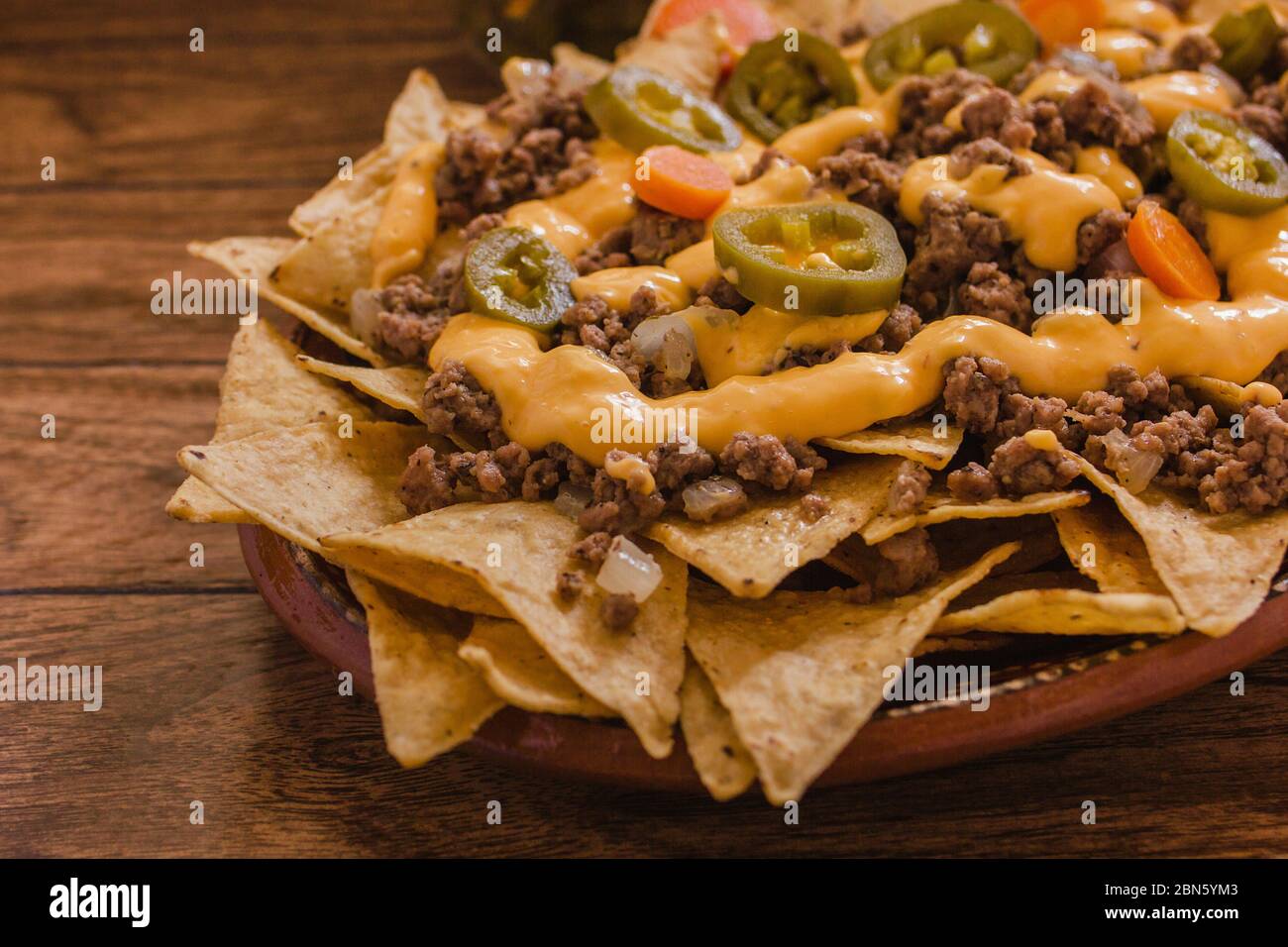 nacho chips corn garnished with ground beef, melted cheese, chili peppers in plate on wooden