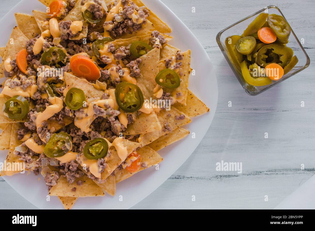 nacho chips corn garnished with ground beef, melted cheese, chili peppers in plate on wooden