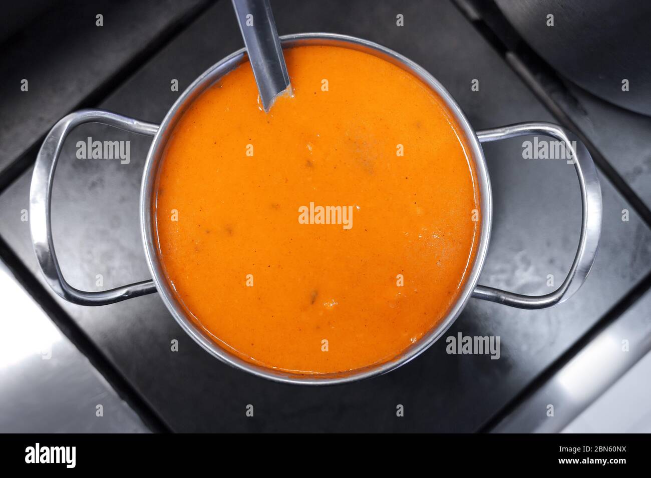 Yellow thick soup in a metal pot on the stove. Style and minimalism in the kitchen design. Stock Photo