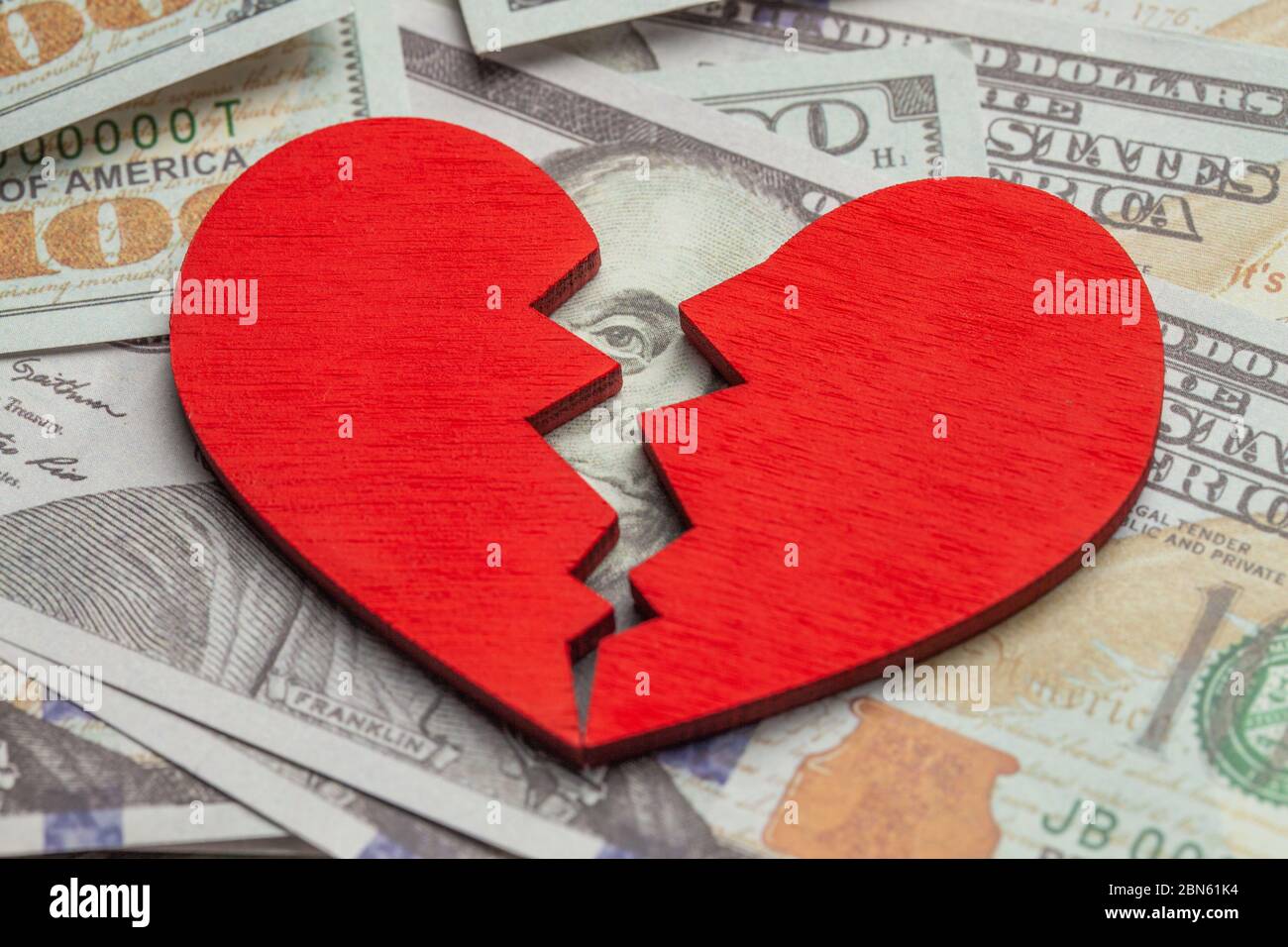 Broken heart because of money. Heart on a stack of cash dollars. Crack in the red heart, Breaking the relationship. Stock Photo