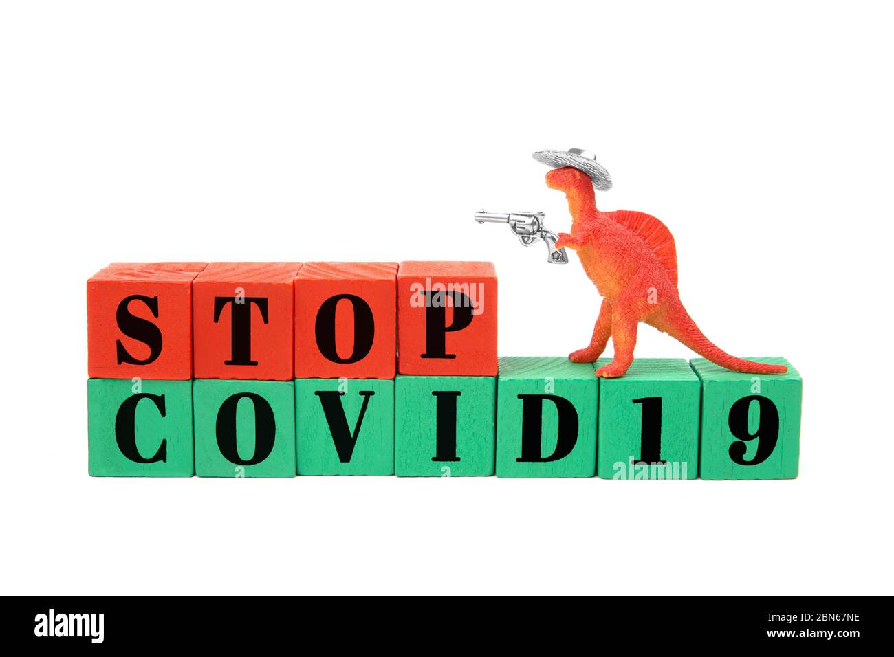 Toy dinosaur T-rex wearing a cowboy hat and holding a shining gun in his arm stands on a line of red and green wooden blocks reading Stop Covid19 Stock Photo
