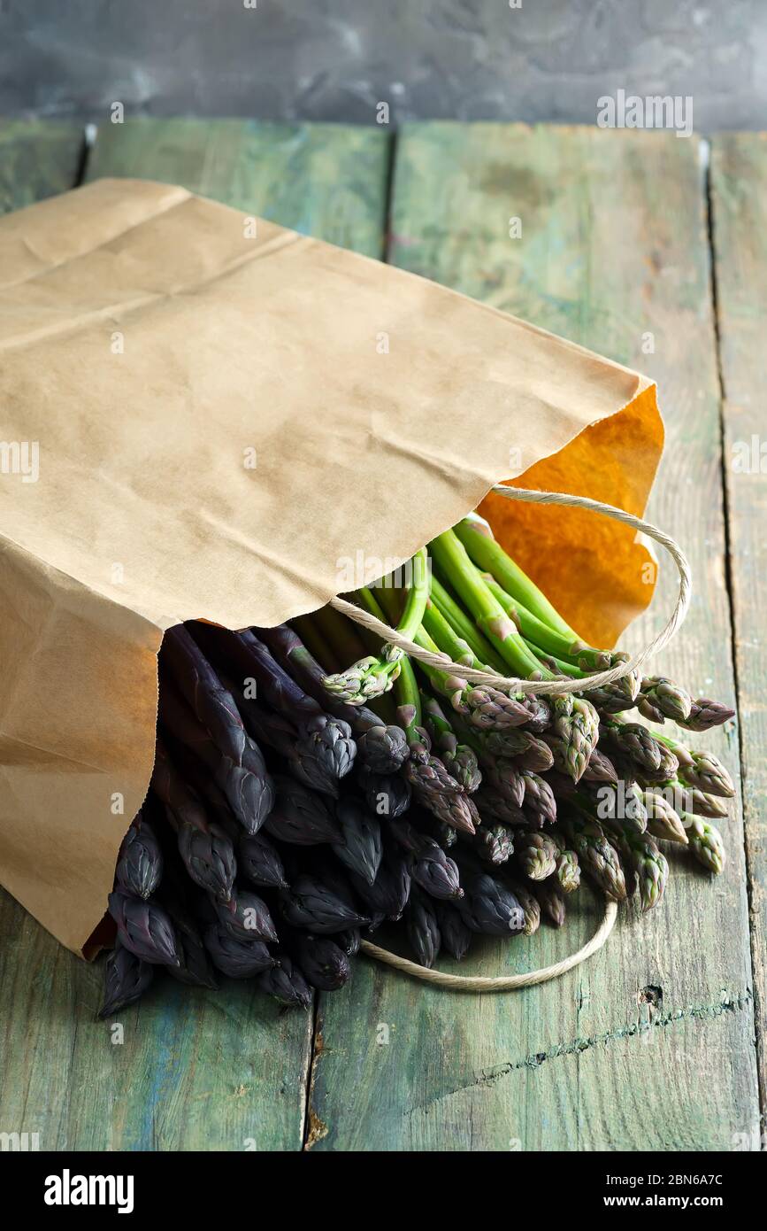 Set with green and purple asparagus in paper bag on old wooden background Stock Photo