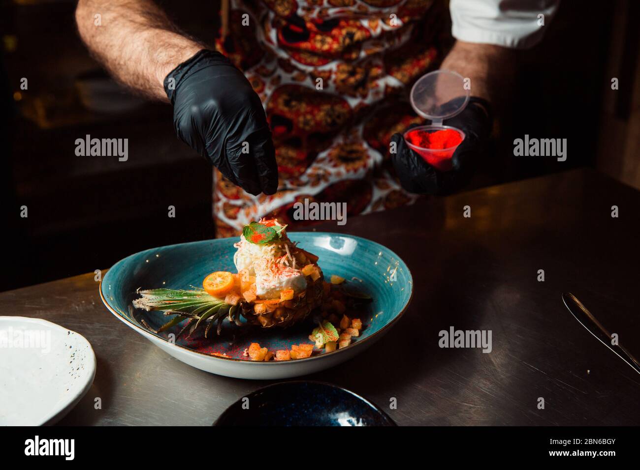 The cook, whose hands are dressed in black gloves, sprinkles the cooked