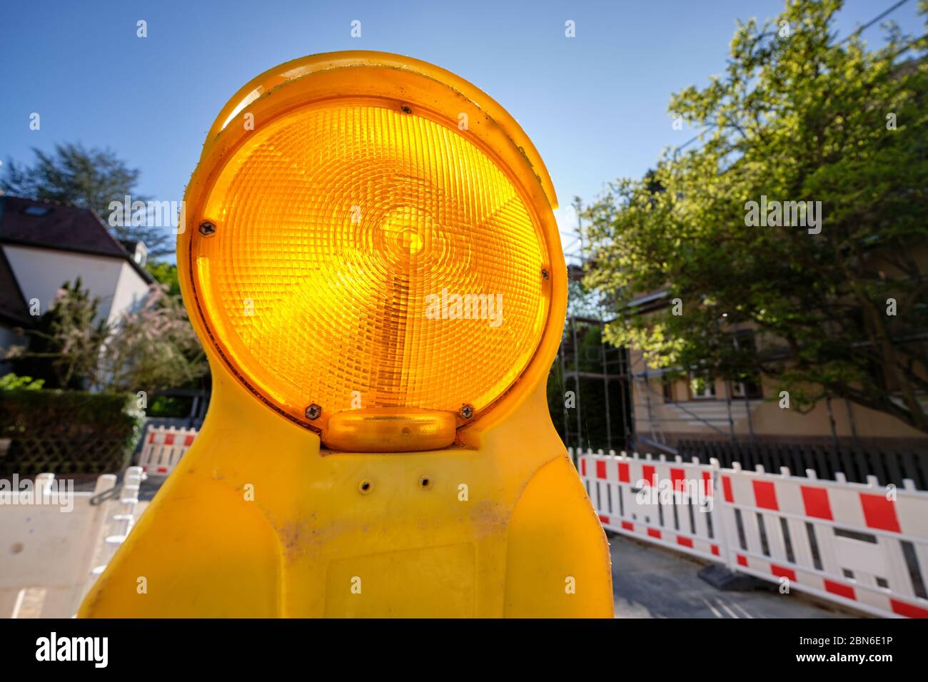 Closeup of a bright illuminated yellow road warning lamp on a construction site in a residential area with blue sky in Germany. Stock Photo