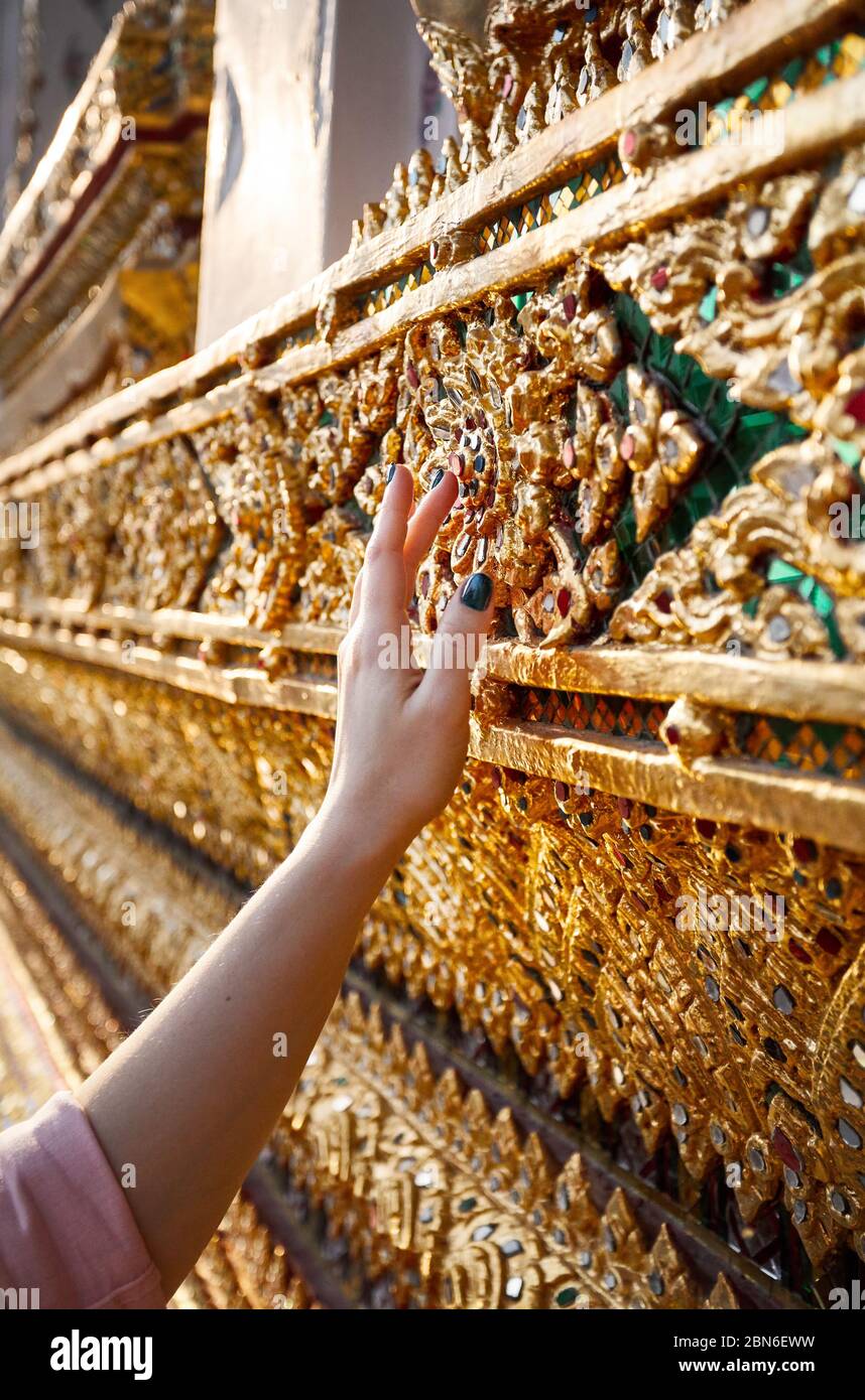 Woman hand is touching Beautiful Decorated wall in Wat Arun temple close up at sunset in Bangkok, Thailand. Stock Photo