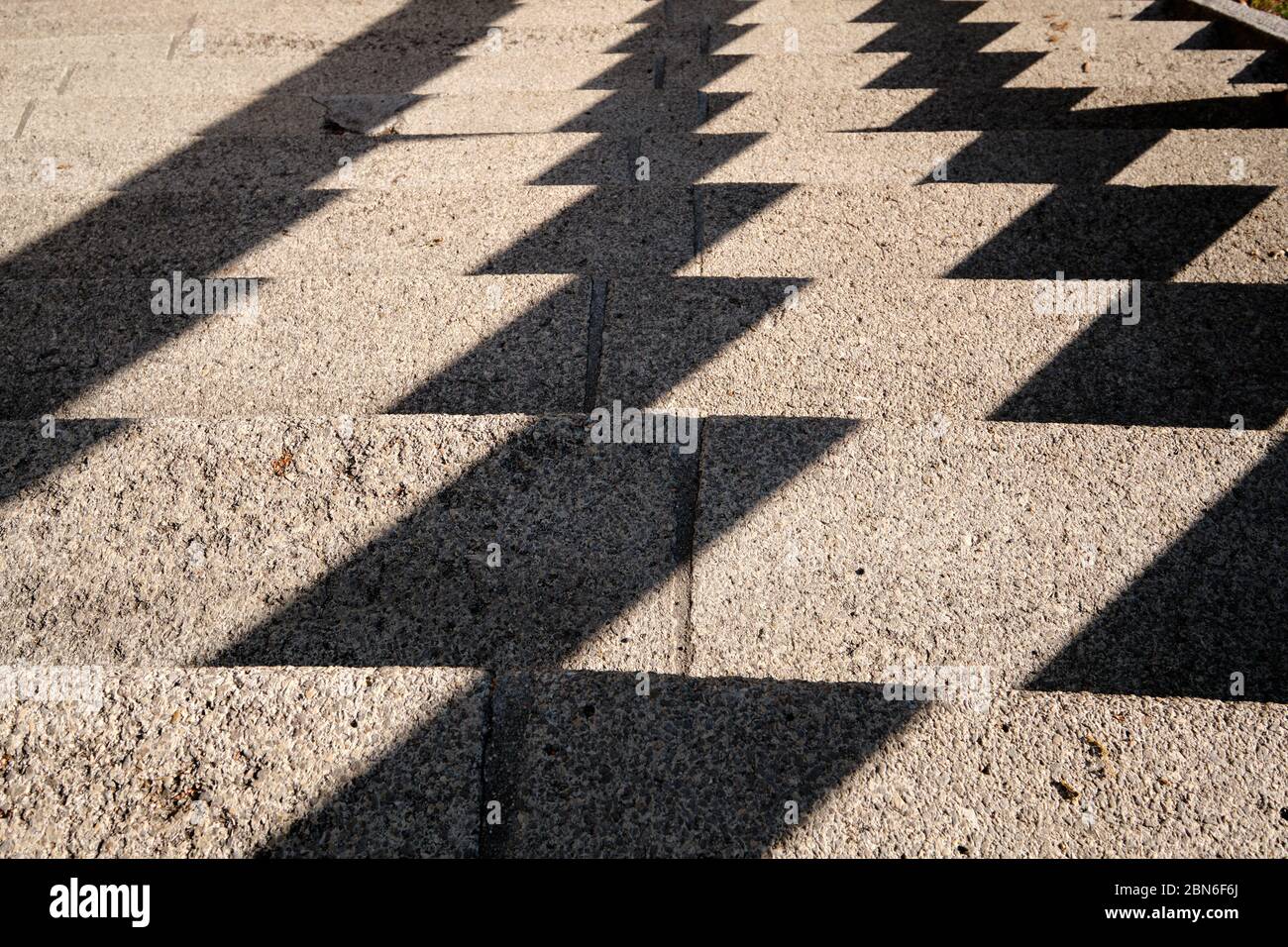 Abstract background shot with a pattern created by harsh shadows on a concrete staircase in the city. Seen in Germany in May. Stock Photo