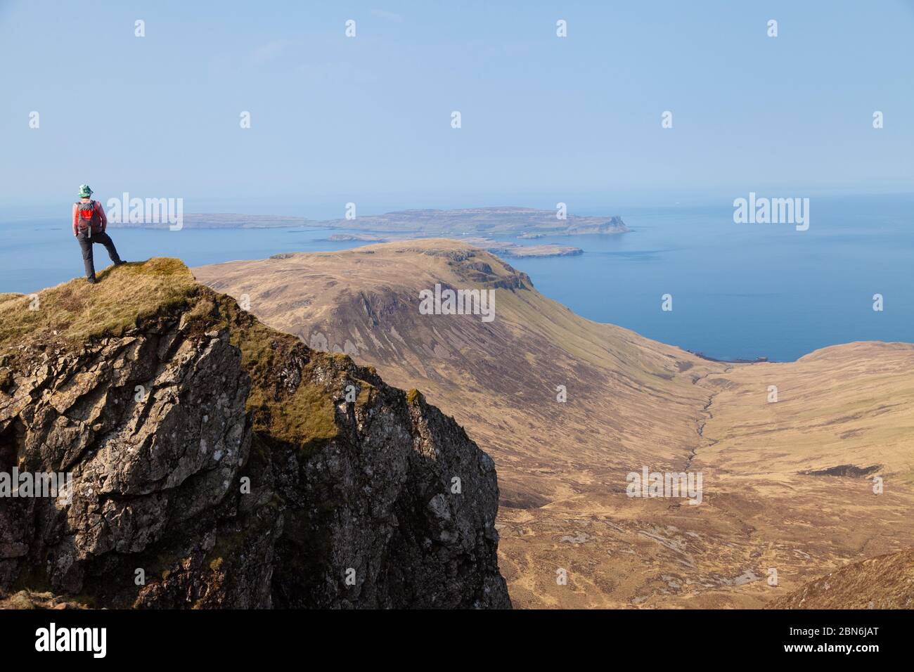 A walker standing on a rocky outcrop on the mountain Orval on the Isle of Rum, looking towards the islands of Canna and Sanday Stock Photo