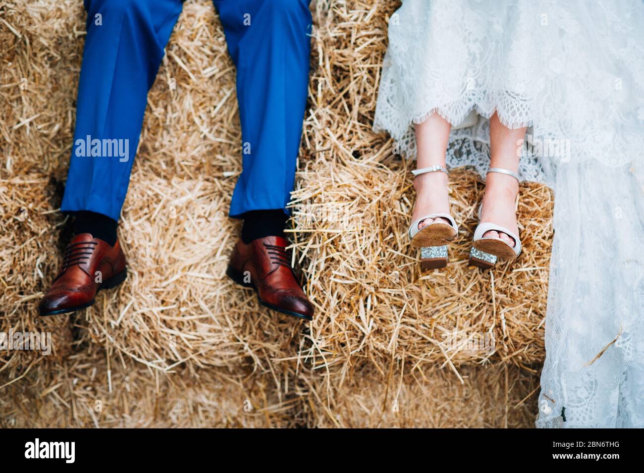 Bride & Groom sitting on a haystack together, outdoor farm wedding England UK Stock Photo