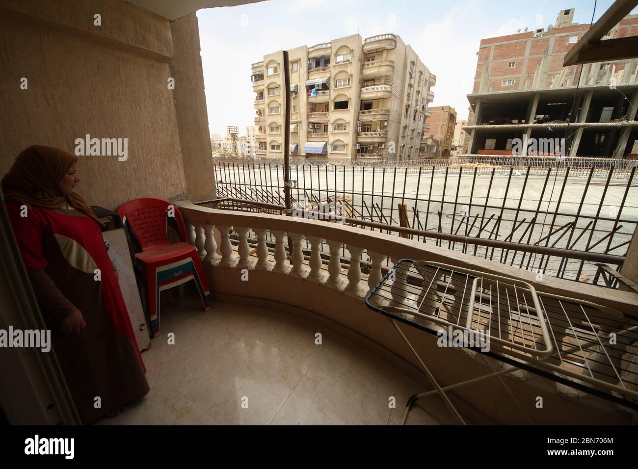 Giza, Egypt. 13th May, 2020. A woman stands in her apartment's balcony overlooking a newly constructed section of a bridge road, locally known as the King Salman Axis, which has been built directly in parallel to residential buildings at Al Omraniya district, leaving very little space between the road and the tower blocks. Credit: Sayed Hassan/dpa/Alamy Live News Stock Photo