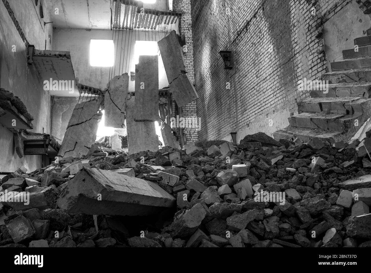 Black and white image. Destroyed concrete building inside with a pile