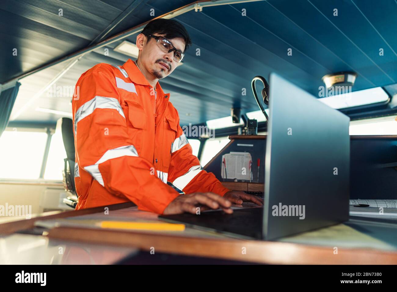 Filipino deck Officer on bridge of vessel or ship. He is using laptop ...