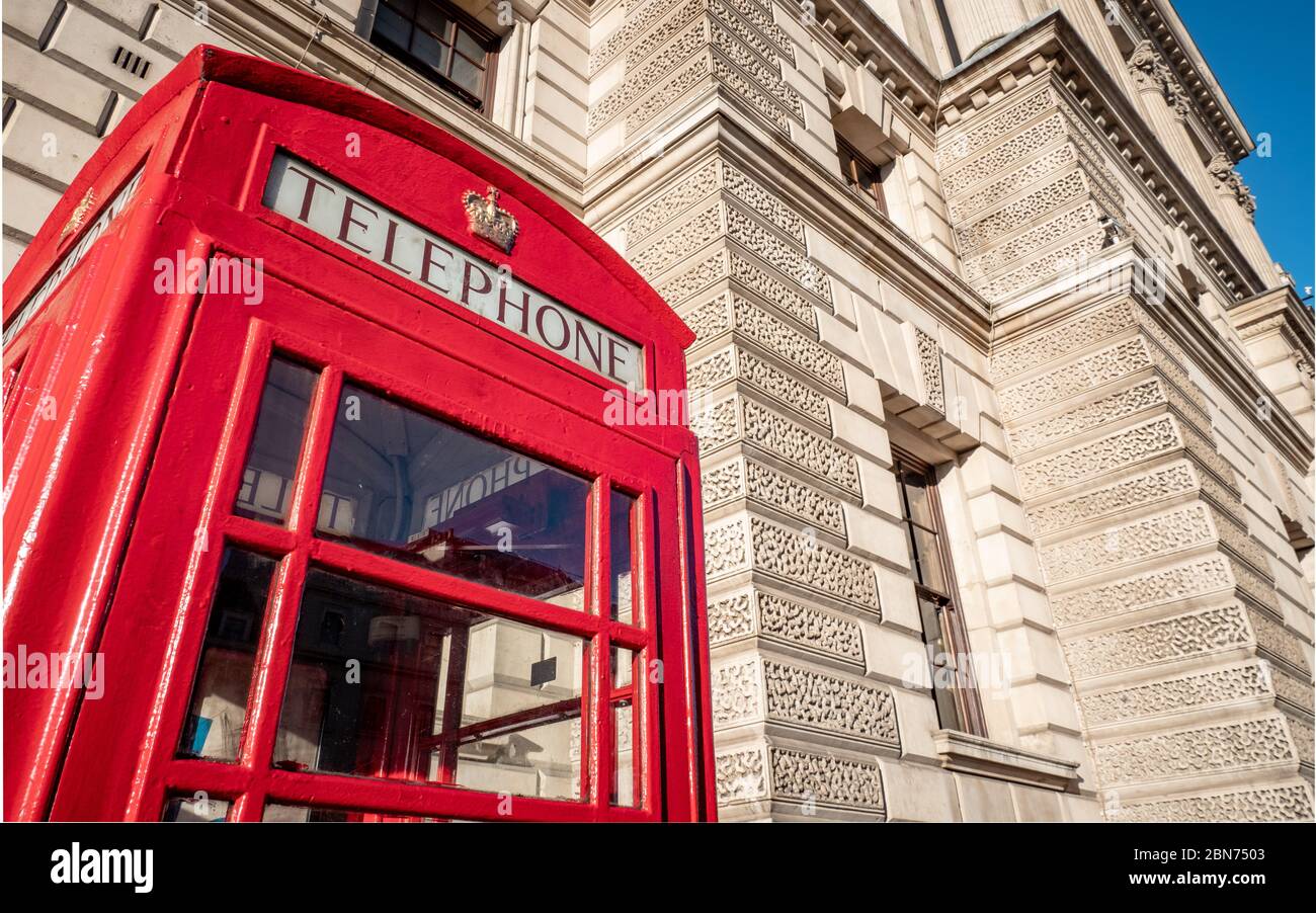 A traditional old red UK telephone box outside one of the many government buildings in Whitehall, London. Stock Photo