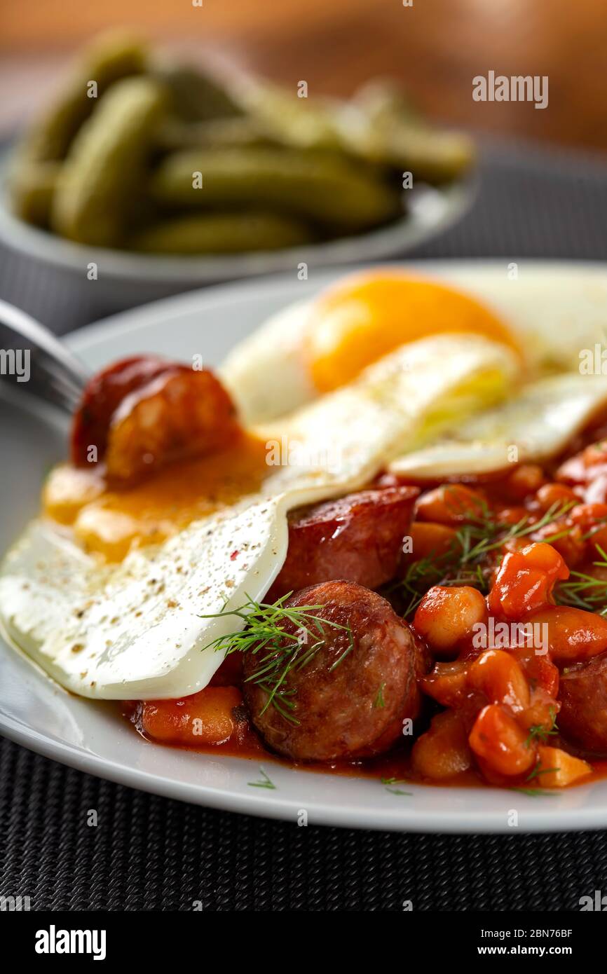 Eating fried eggs with beans and pork sausages - close up view Stock Photo