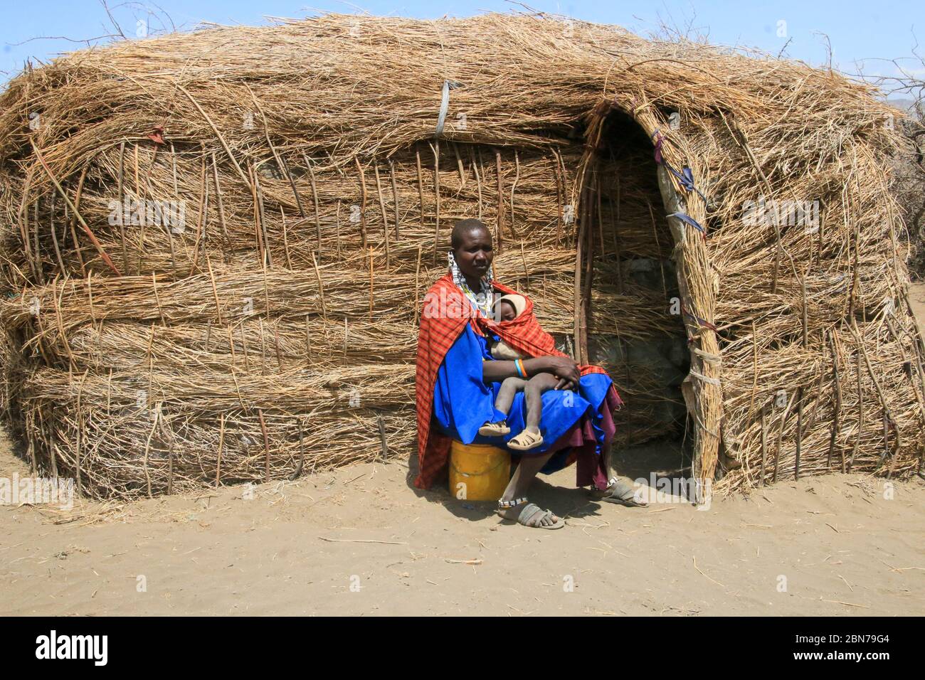 Maasai Woman and baby sit in front of her mud and straw hut. Maasai is an ethnic group of semi-nomadic people. Photographed in Tanzania Stock Photo